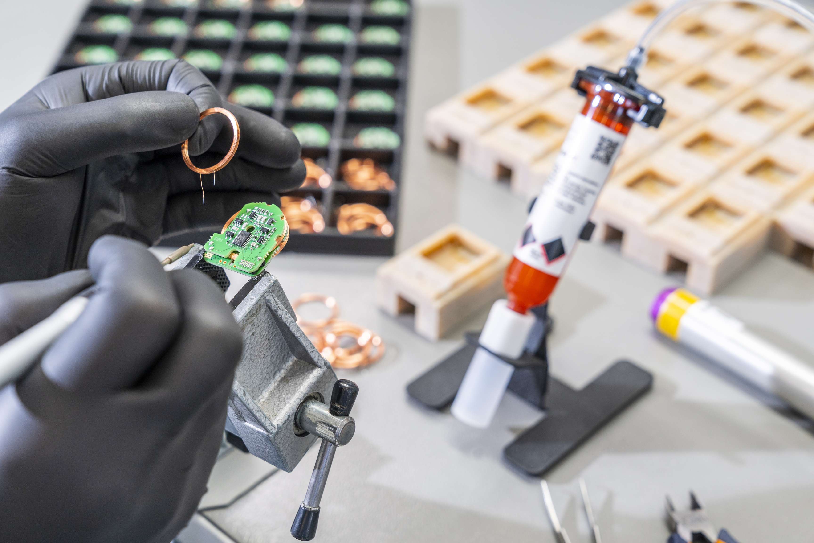 Zwei behandschuhte Hände verrichten beim Zusammenbau der Sensoren eine äußerst filigrane Arbeit.