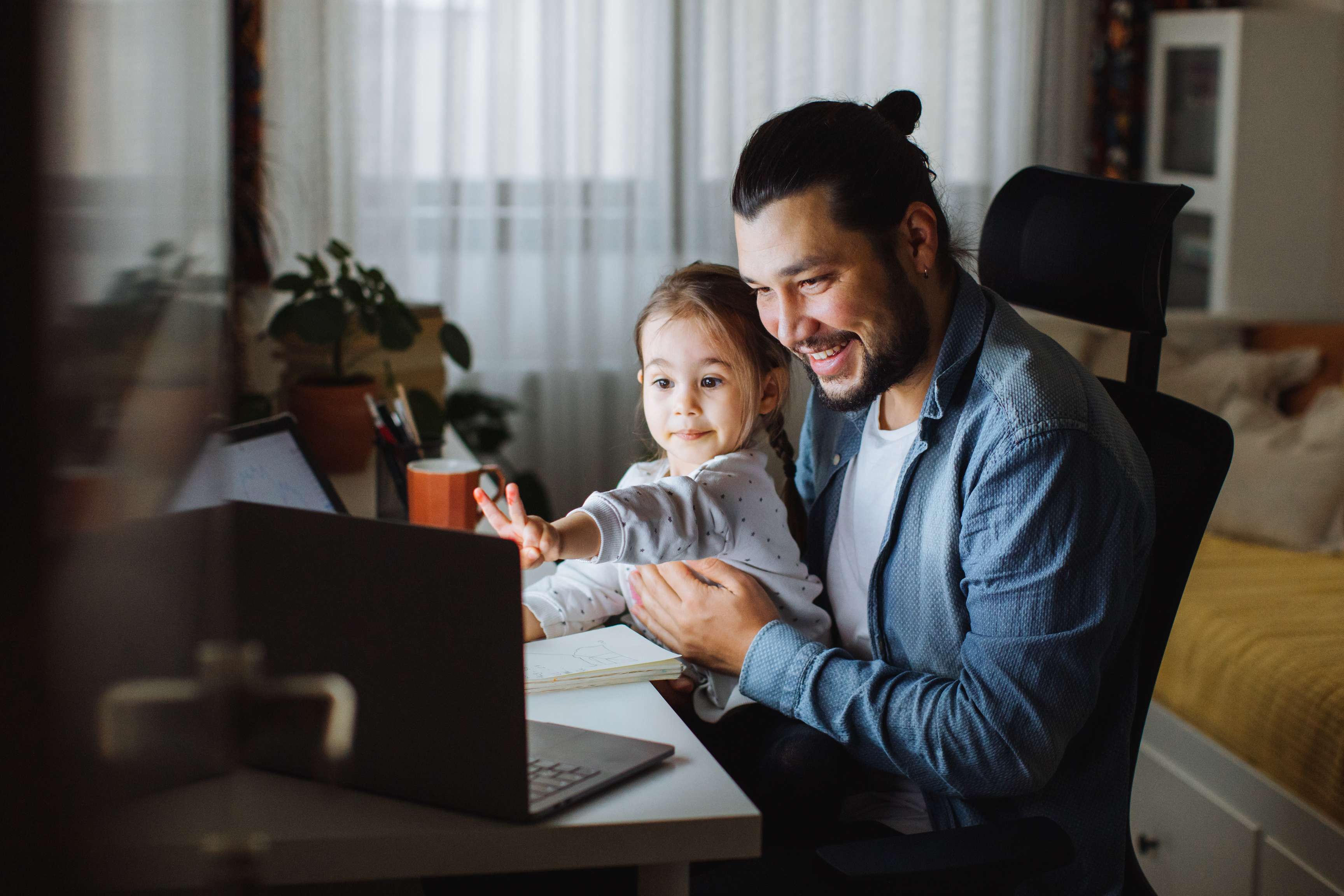 A man with his daughter on his lap in front of a laptop in the home office.