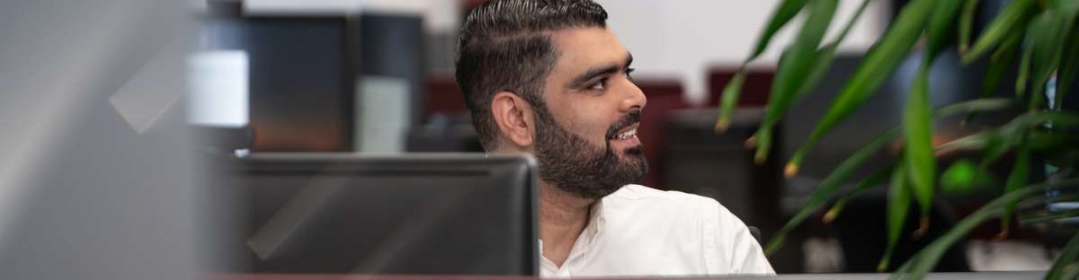 Ein Mann sitzt an einem Schreibtisch und schaut zur Seite.