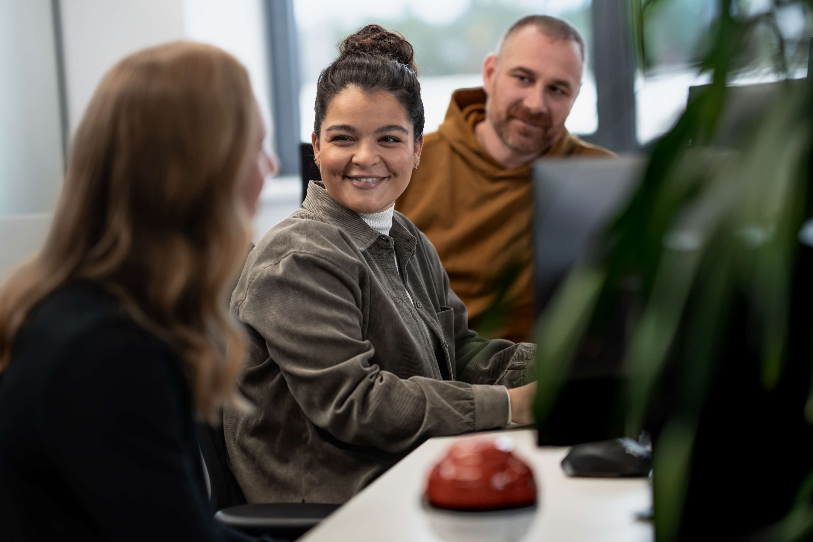 Zwei Frauen und ein Mann sitzen an einem Schreibtisch und unterhalten sich.