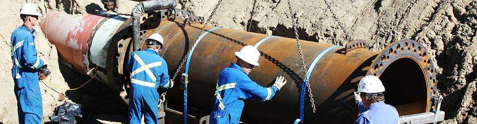Several workers at a pipeline opening in a pit.