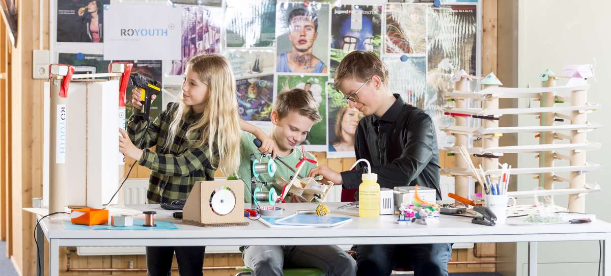 Drei Kinder, die an einem Tisch verschiedene Experimente durchführen oder Dinge basteln.