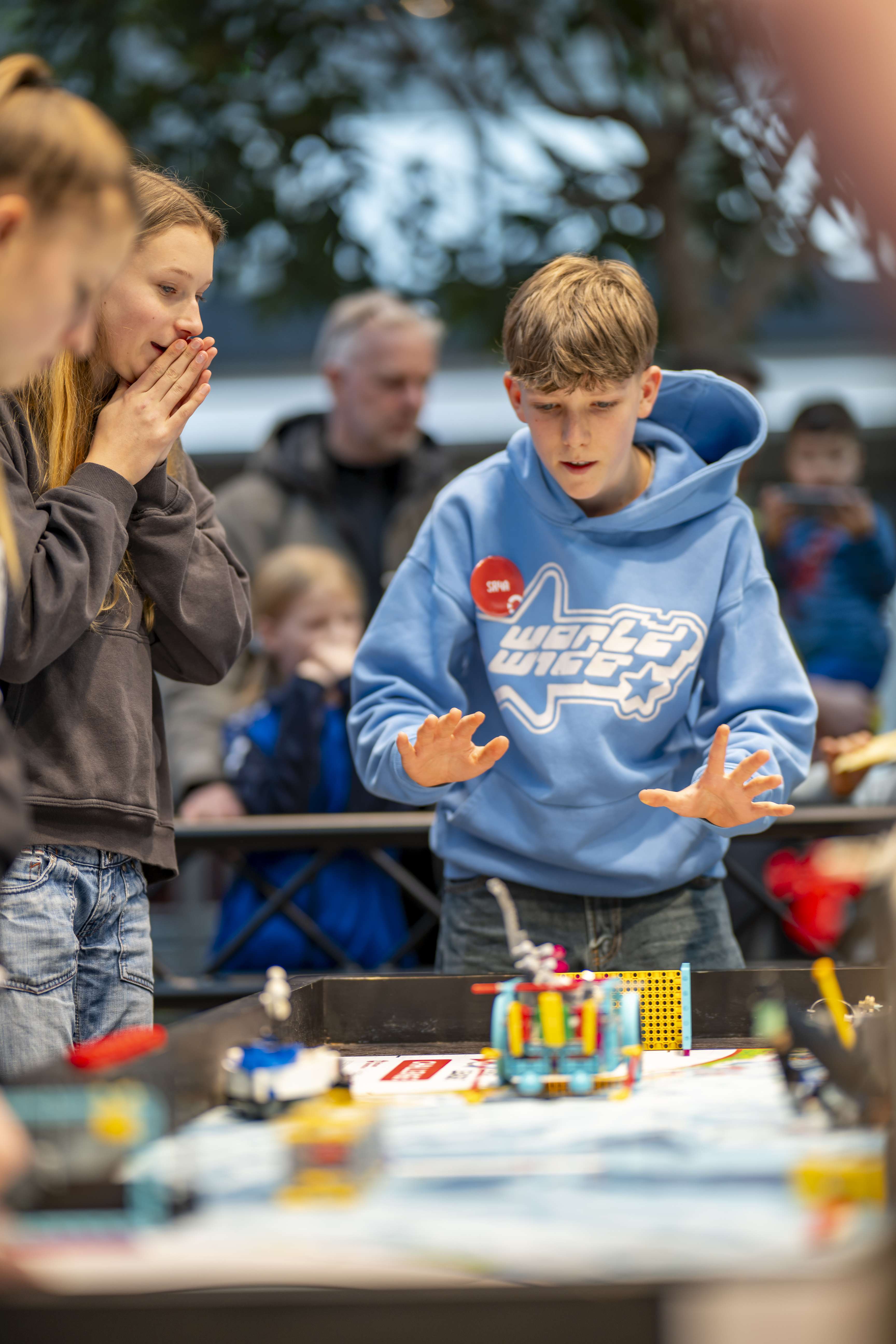 A group of students are standing excitedly in front of a table with LEGO robots.