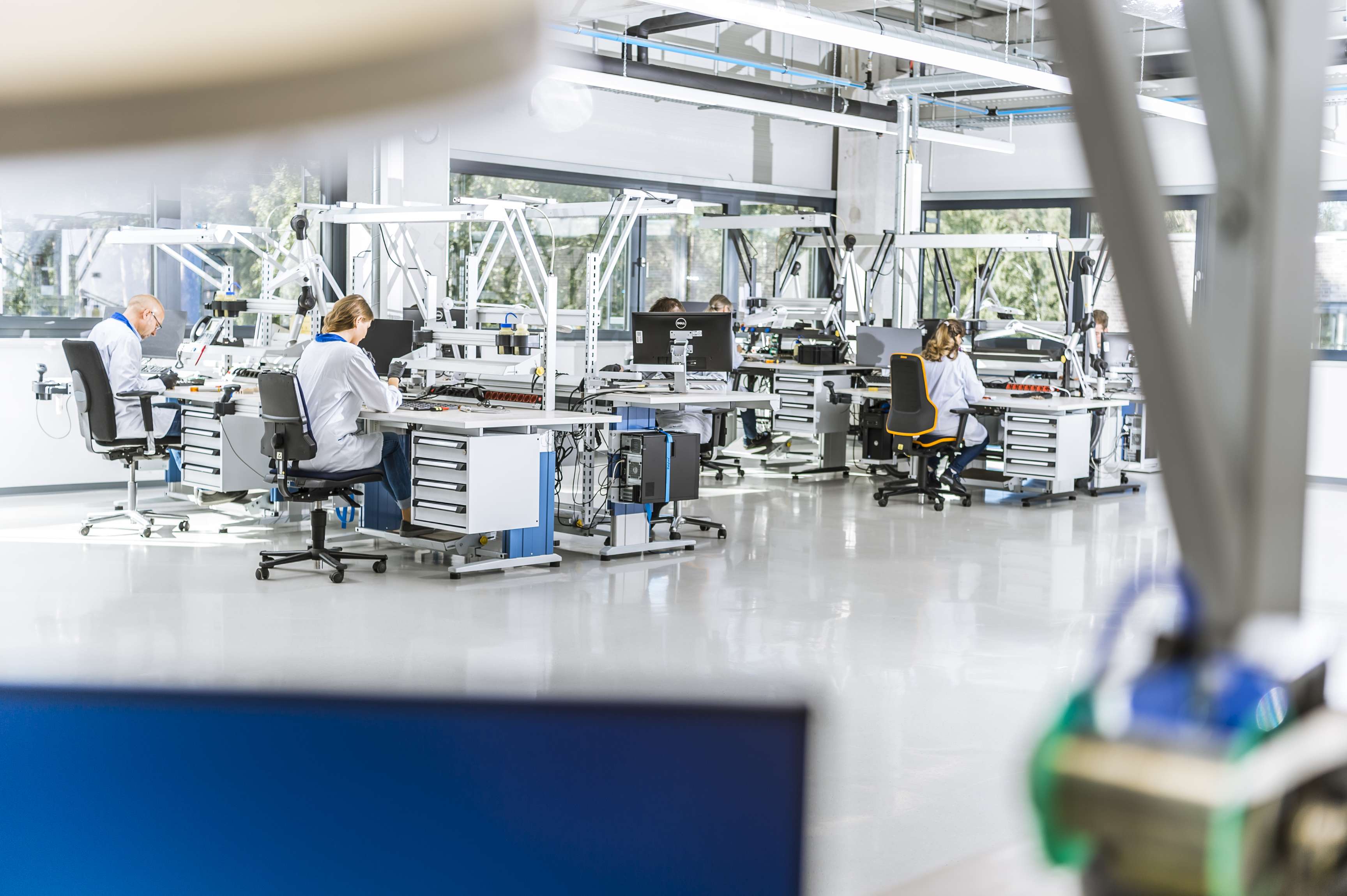 Several people in lab coats sit at their highly specialized workstations and assemble, among other things, circuit boards.