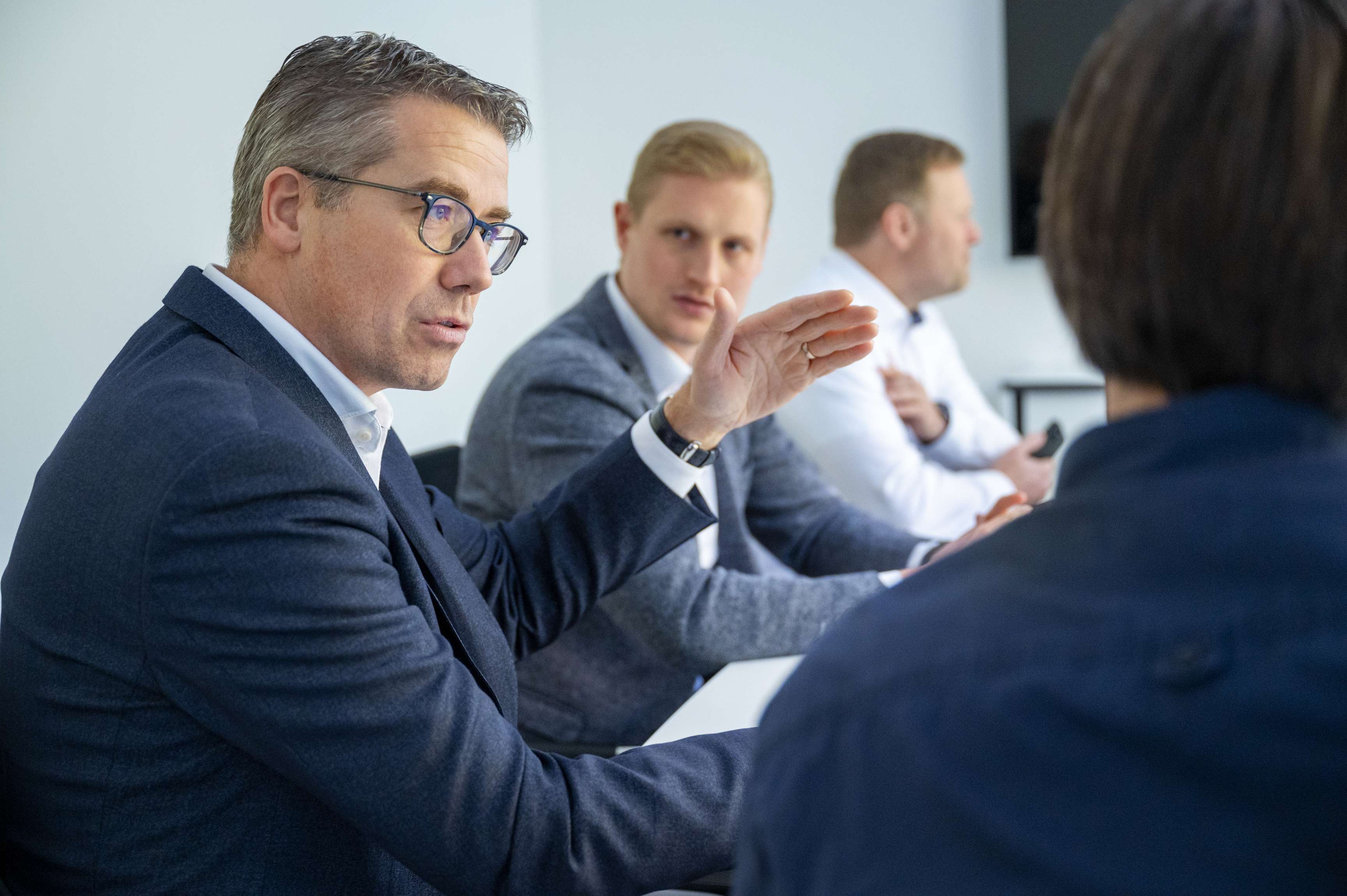 Several employees in suits talking in a meeting in a conference room.