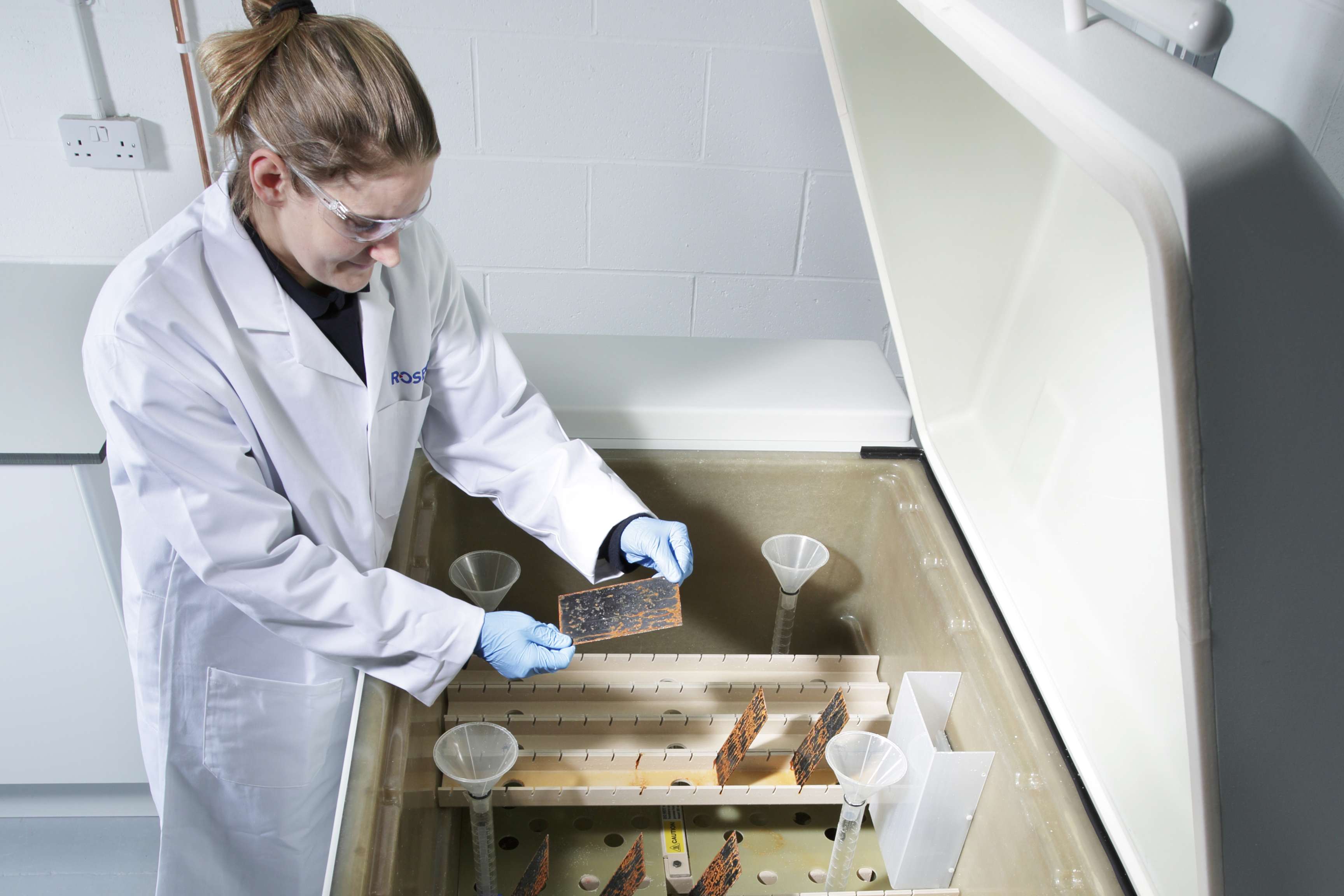 Laboratory employee with protective goggles looks at small glass plate.