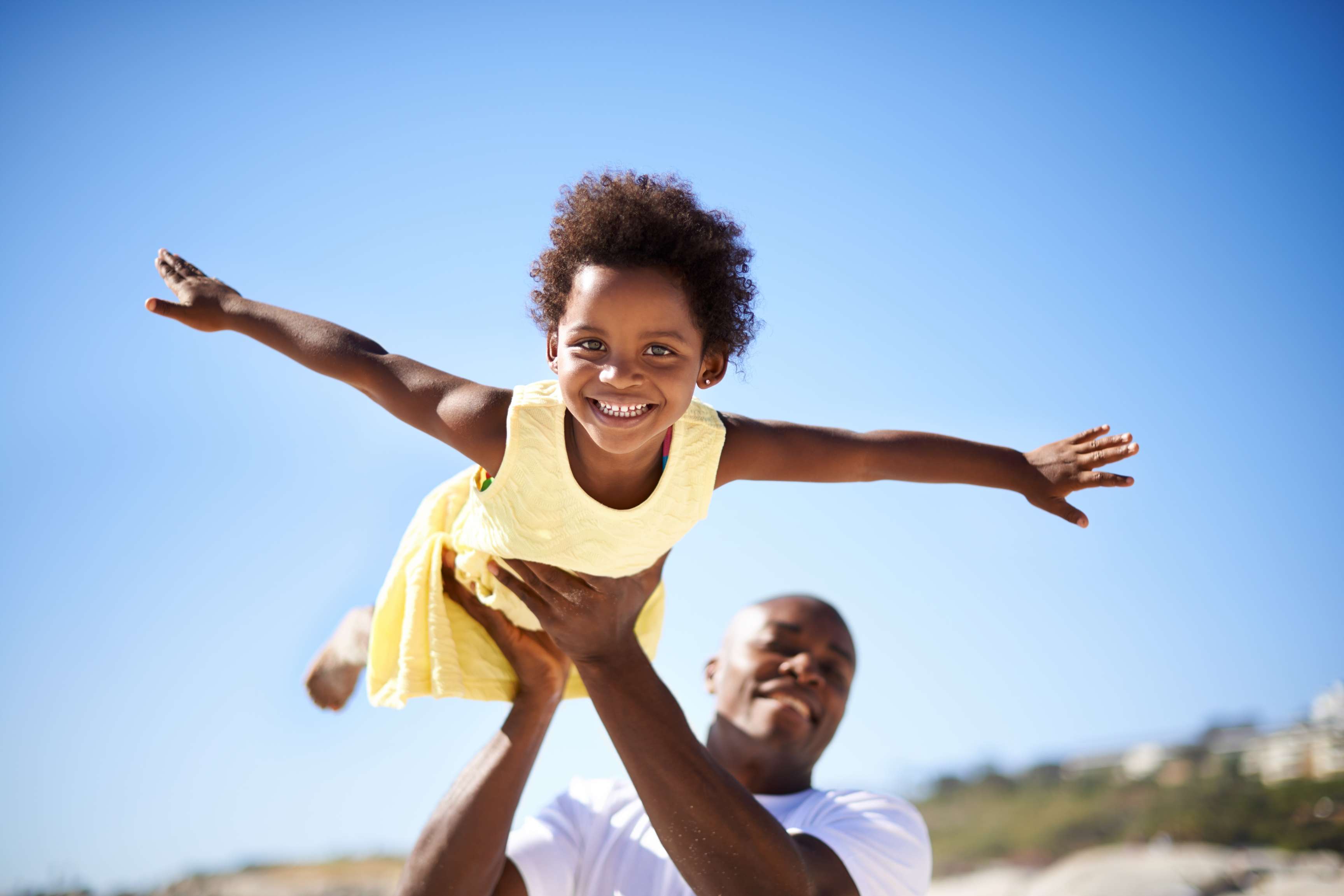 A man holds up his child and the child pretends to fly; both laugh and have fun.