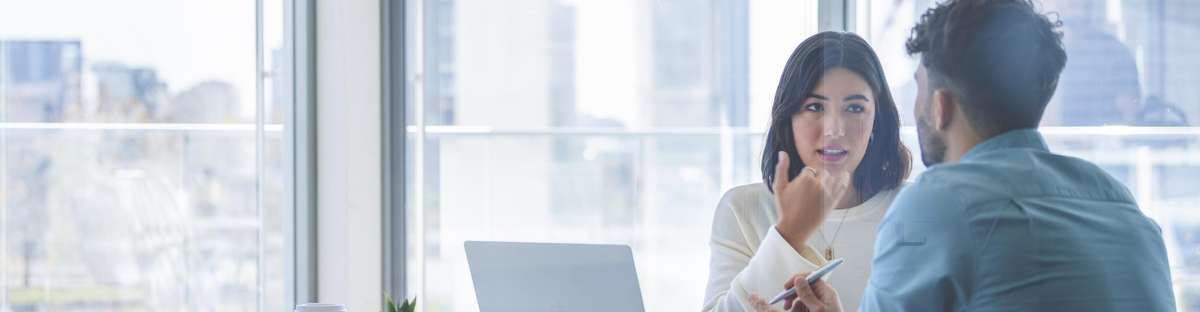 Two people sitting in a meeting room talking to each other.