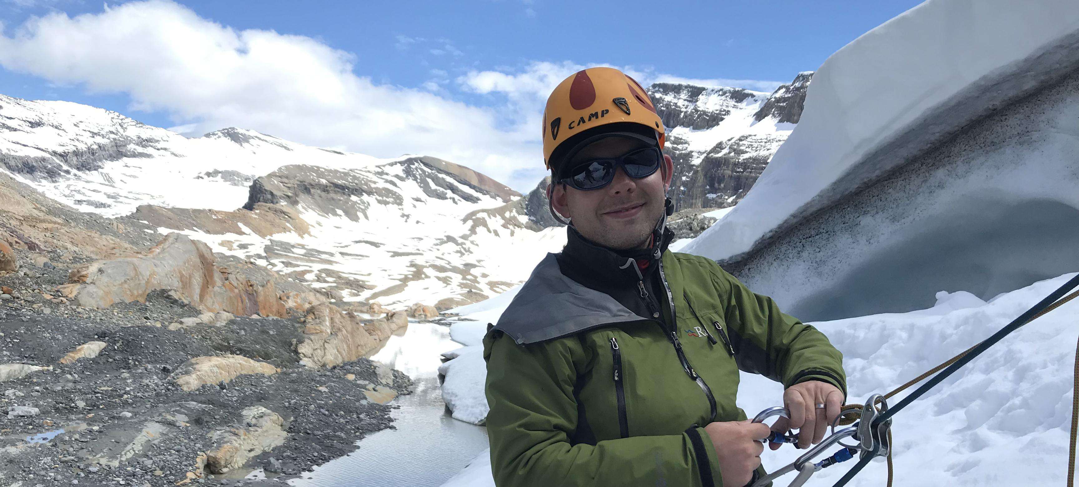 Man with sunglasses smiles at camera while climbing in Rocky Mountains.