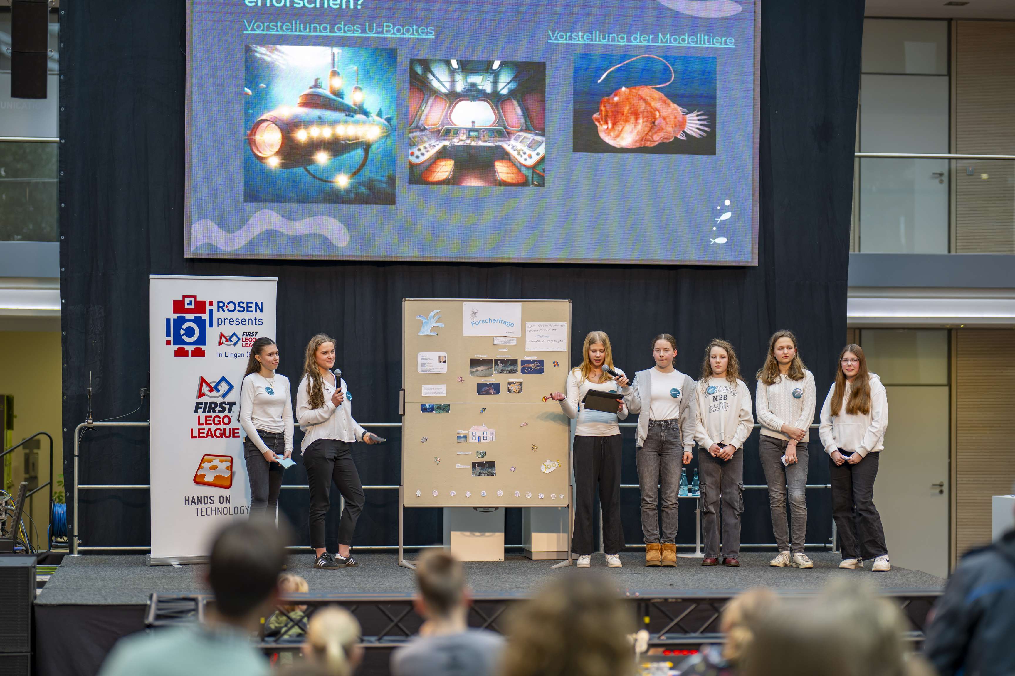 A group of girls present the results of their research project on stage in front of an audience.