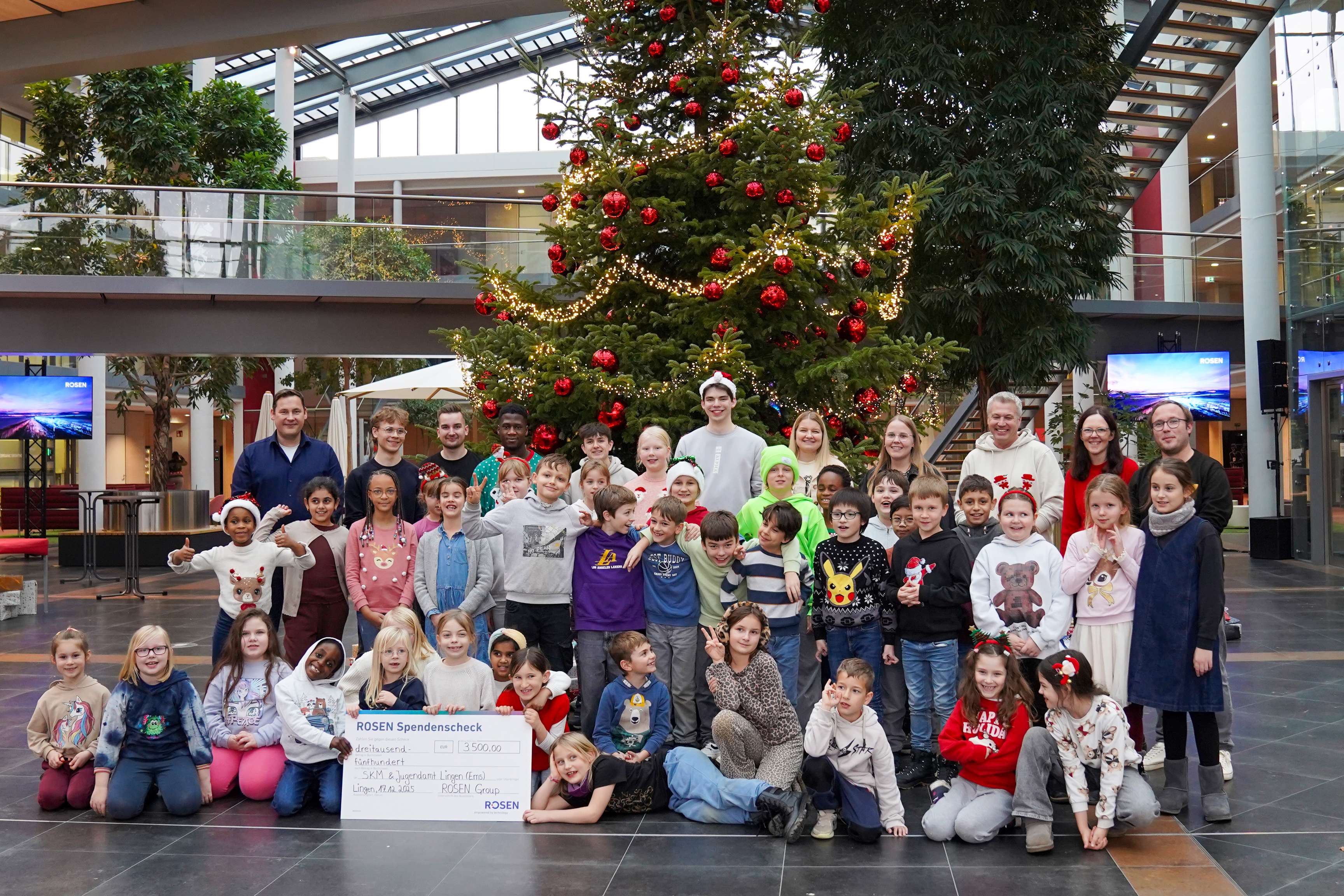Many people (children and adults) in front of a Christmas tree at the donation handover.