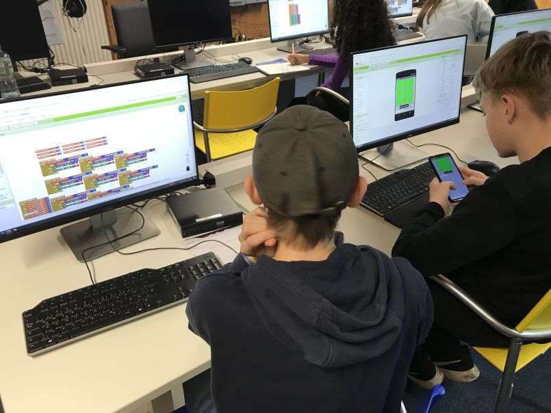 Two students sitting in front of computers building an app