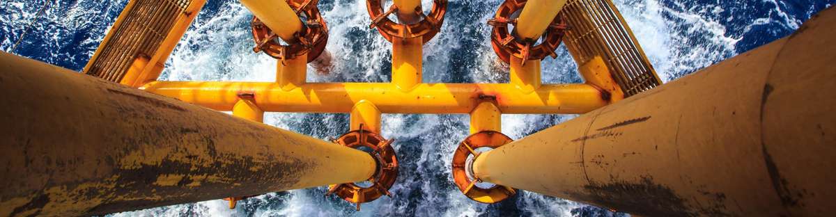 Bird's eye view of vertical yellow pipelines leading into the rough ocean.