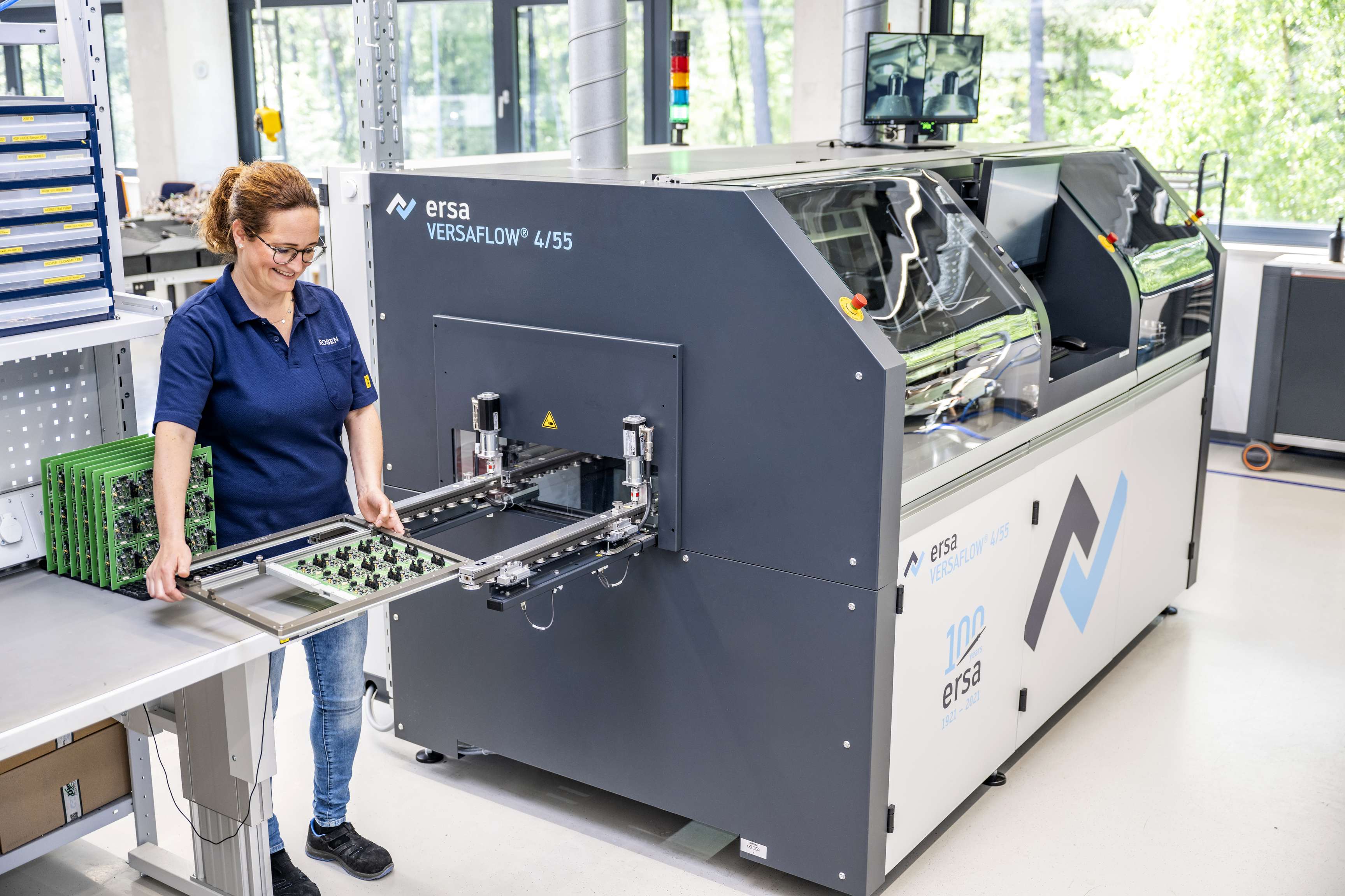 Eine ROSEN Kollegin steht neben einer Lötmaschine für Leiterplatten in der Produktion.