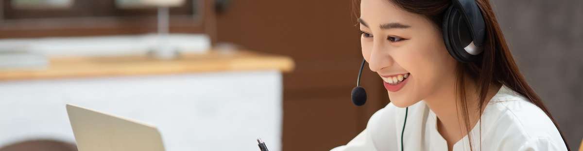 Woman sitting in front of laptop with headset and laughing.