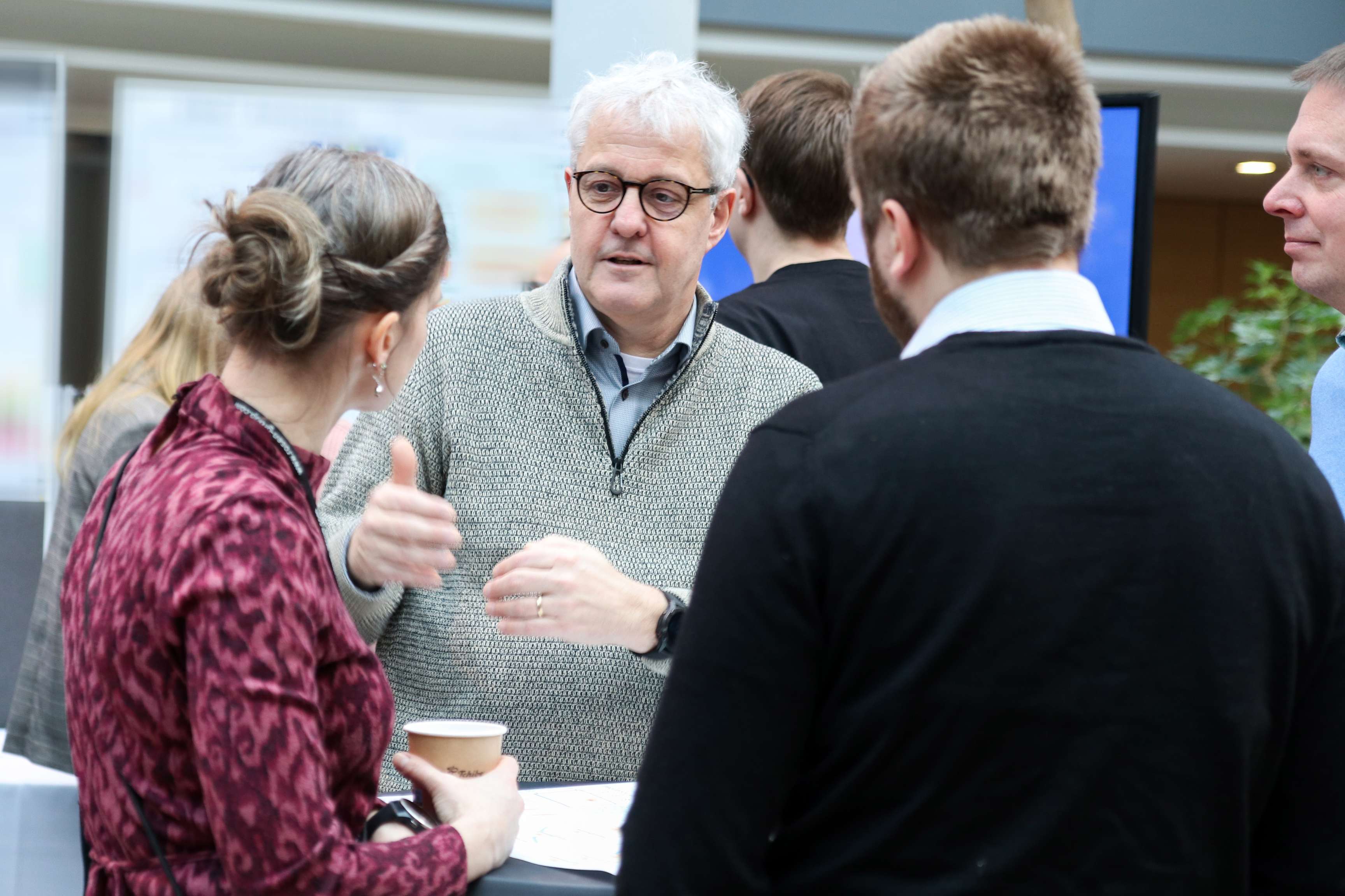 A man is explaining something to his colleagues. They are standing at a bar table.