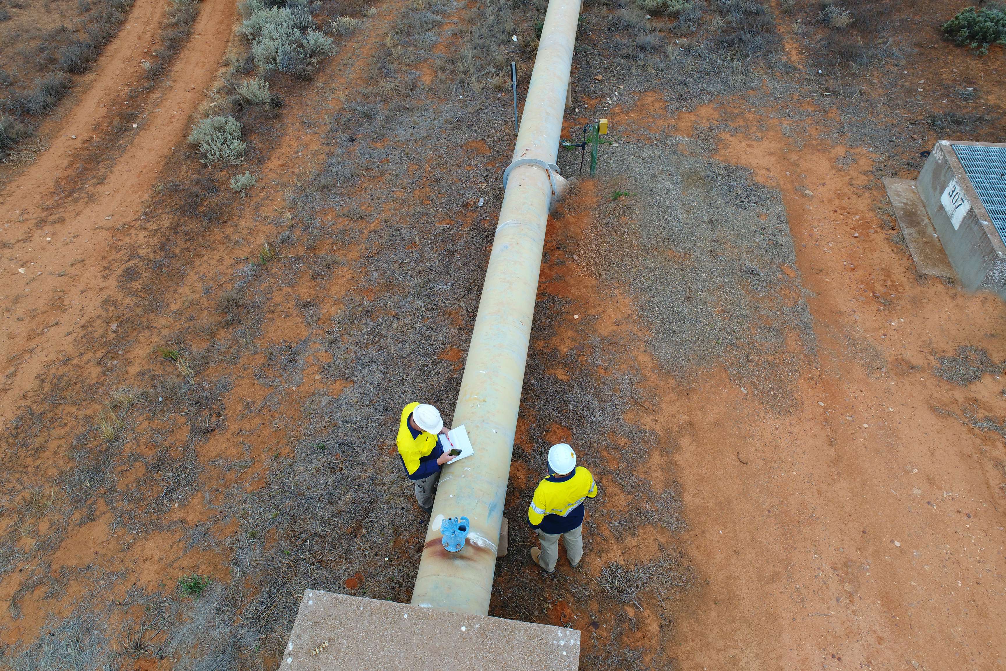 Aerial view of people standing at a pipline.