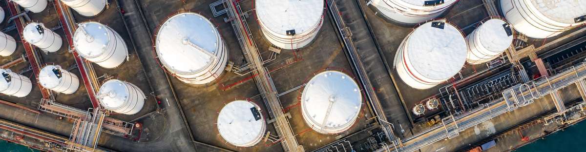 Area of a refinery in which storage tanks of different sizes and a jetty where a ship has docked can be seen. 