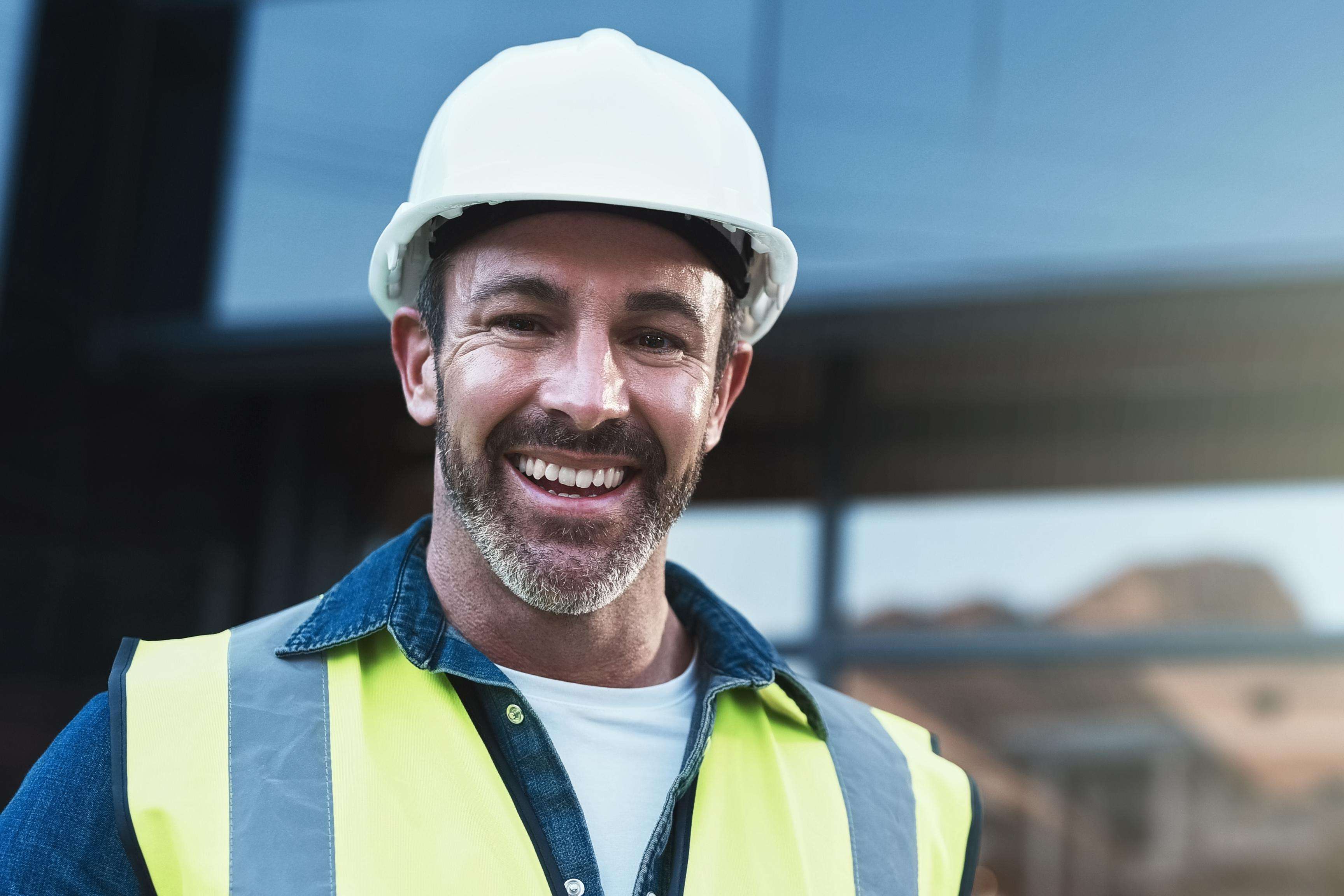 Man wears a safety helmet and other protective clothing while smiling at the camera.