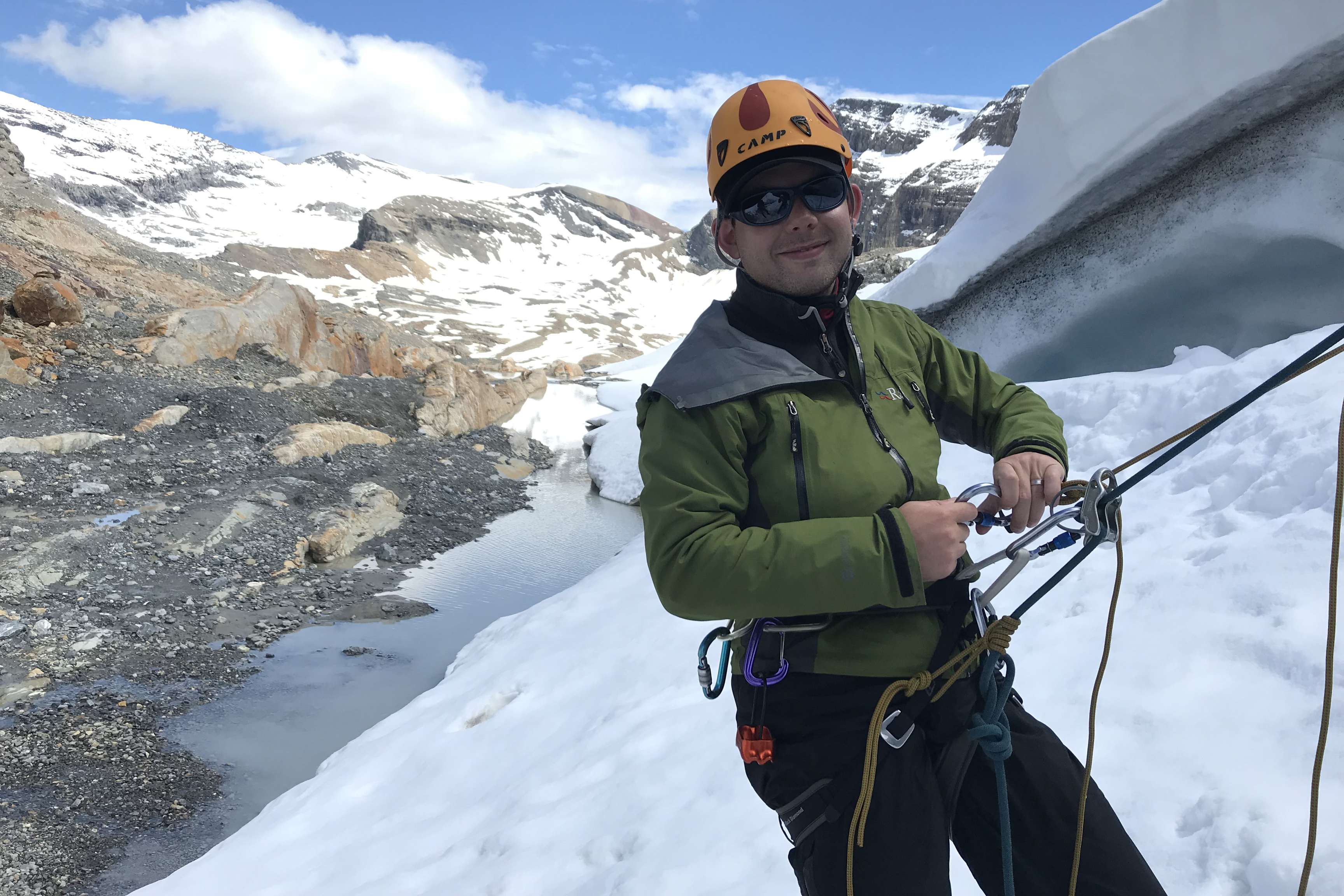 Man with sunglasses smiles at camera while climbing in Rocky Mountains.