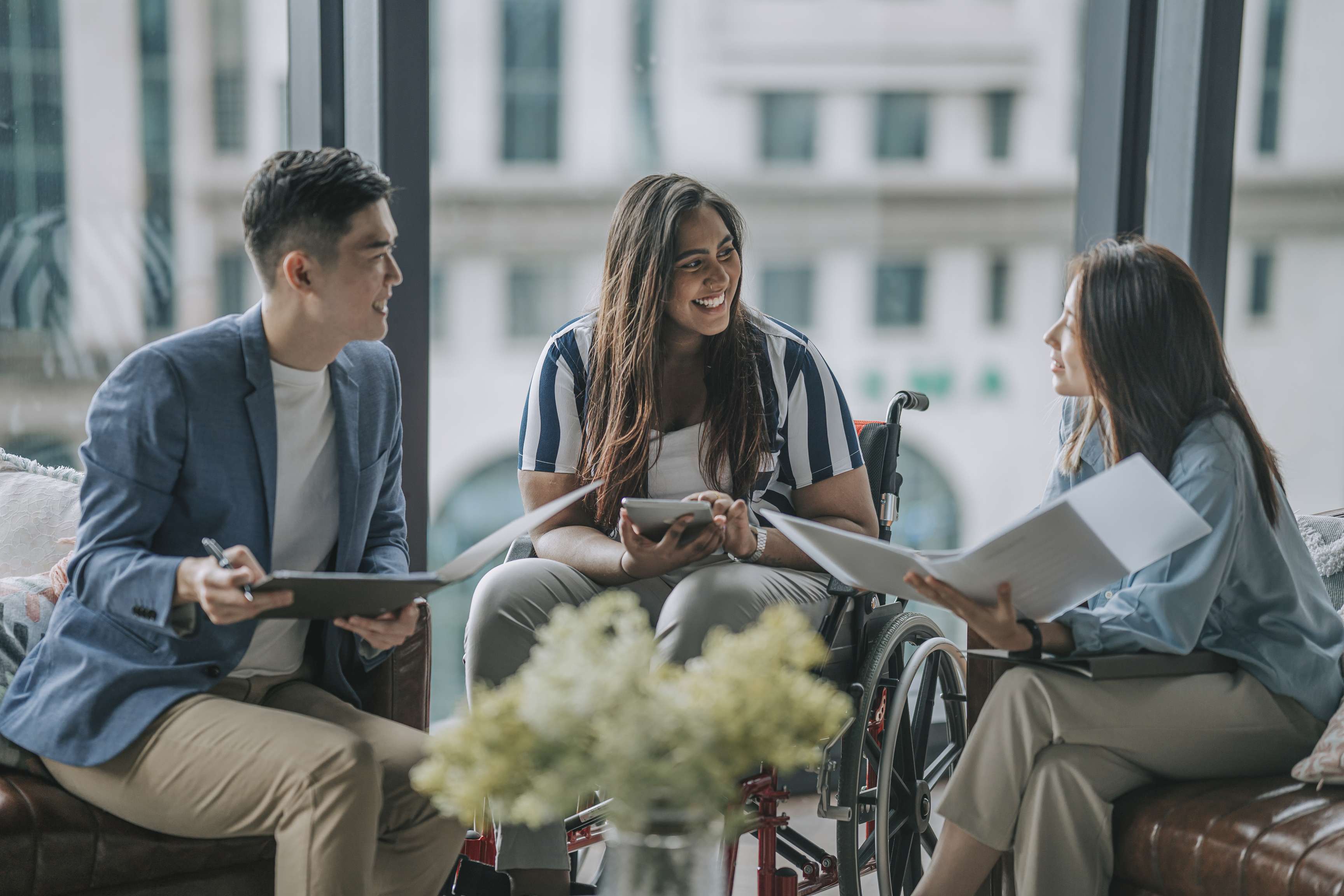 Three people sitting side by side talking to each other, one woman sitting in a wheel chair.