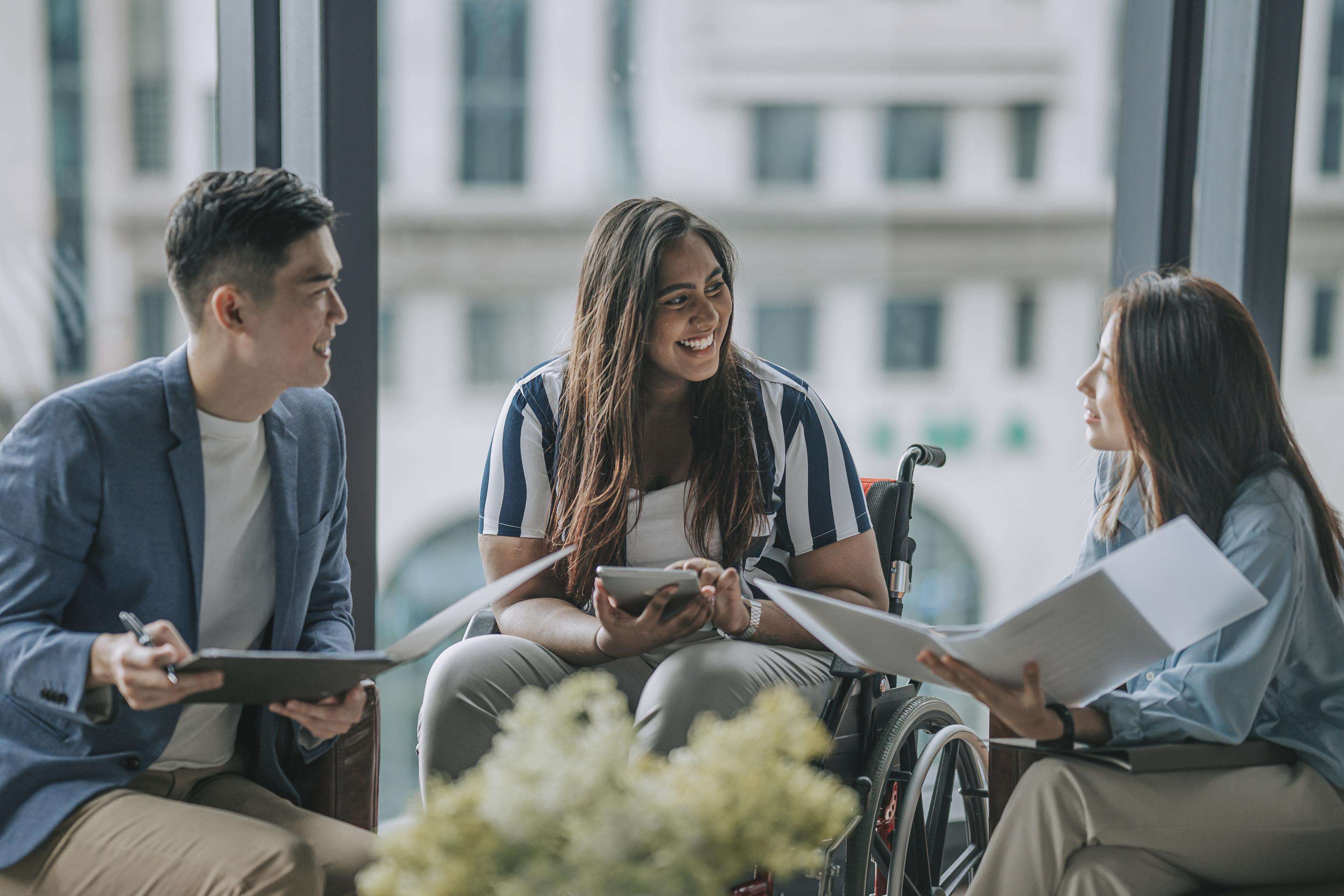 Three people sitting side by side talking to each other, one woman sitting in a wheel chair.