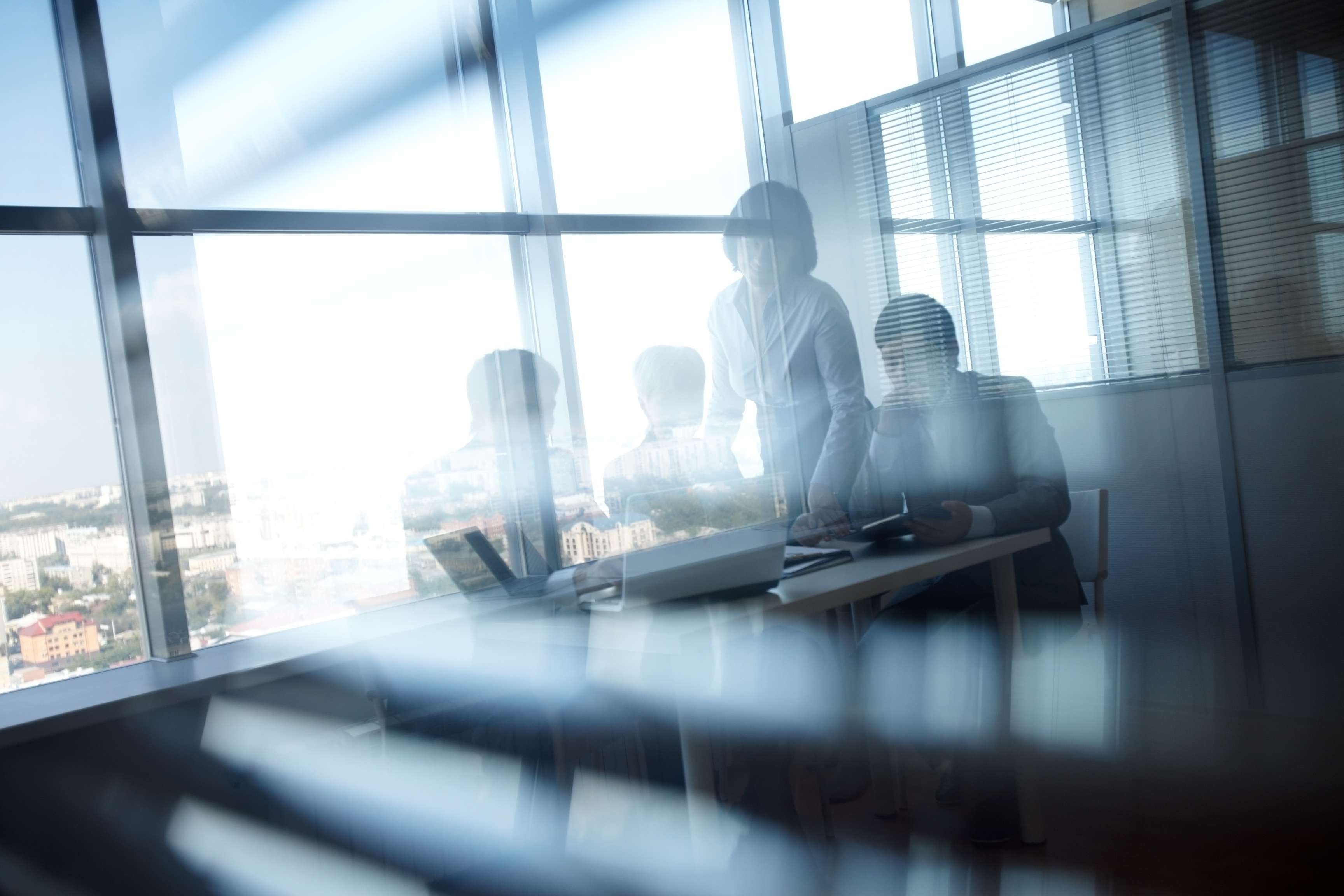 View through glass pane on several people sitting together in meeting room.