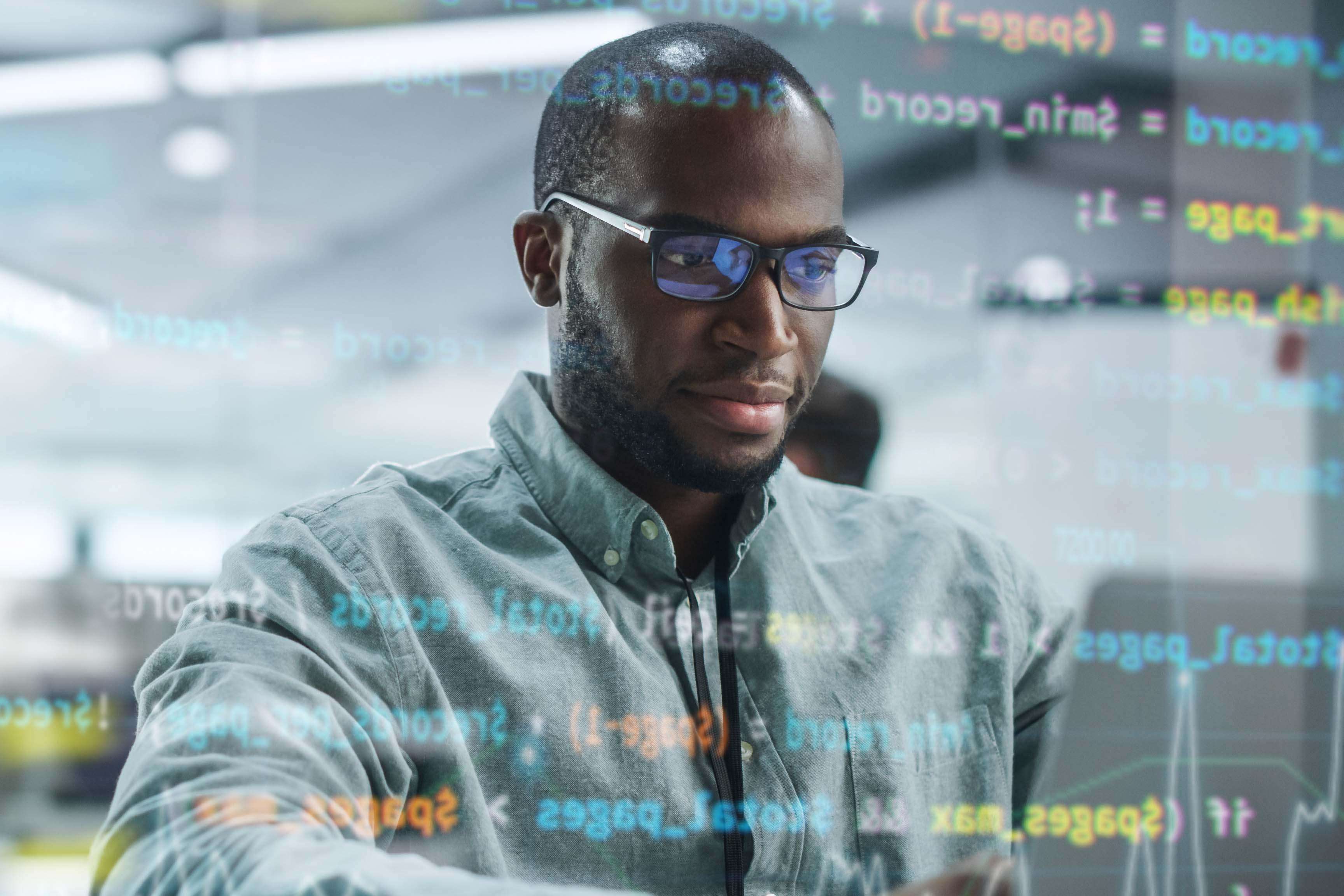Portrait of man with glasses sitting in front of laptop and programming.