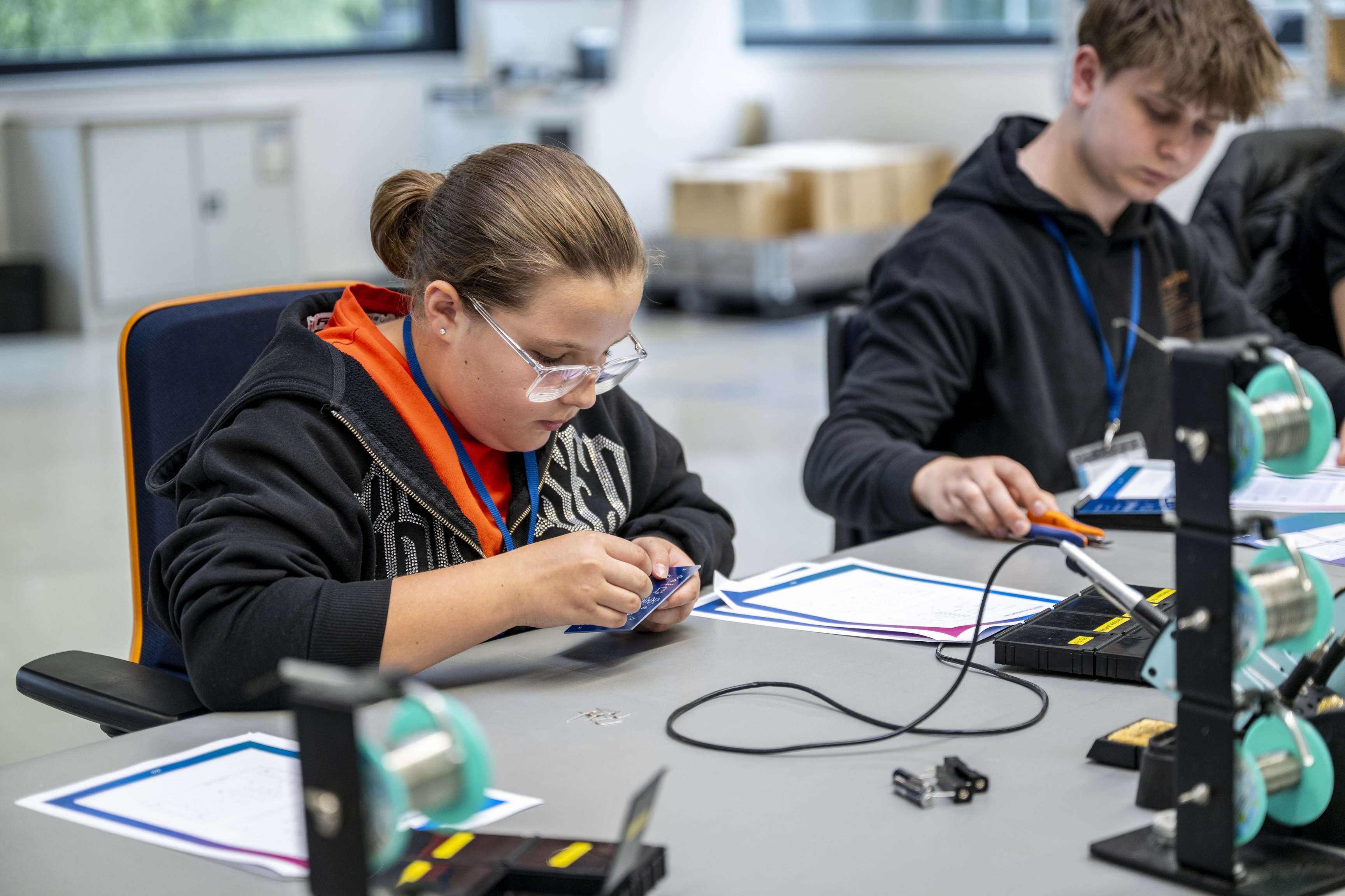 Schüler, die während einer praktischen Schulung an einem Arbeitsplatz elektronische Bauteile zusammenbauen.