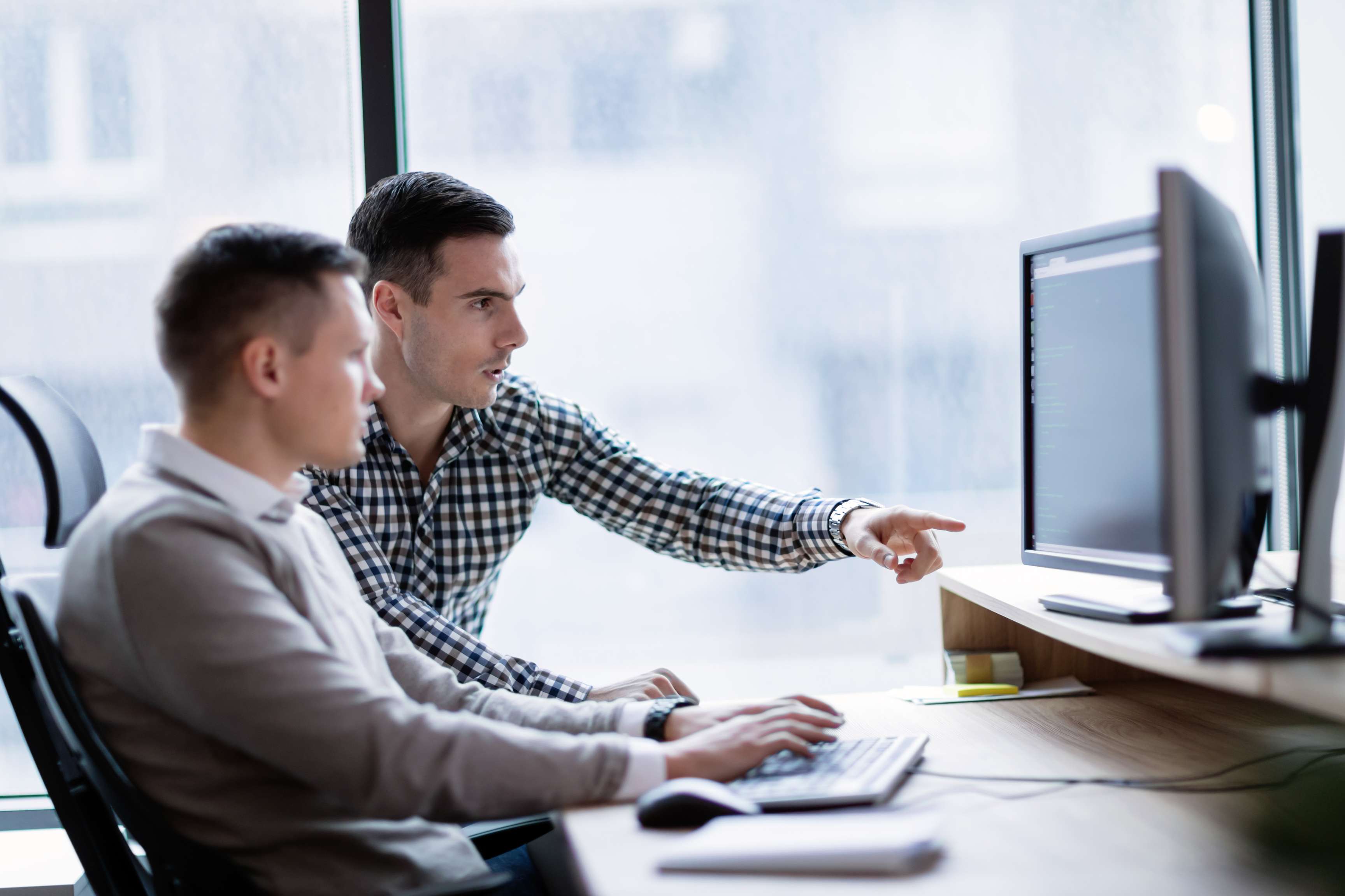 Two employees at an office looking and pointing at a computer screen.