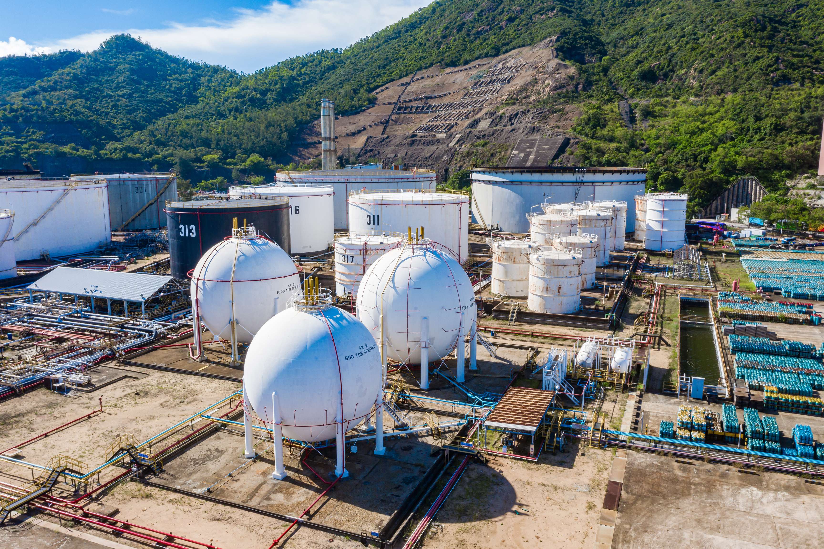 Tank farm with pressure vessels in the foreground and green mountain in the background.