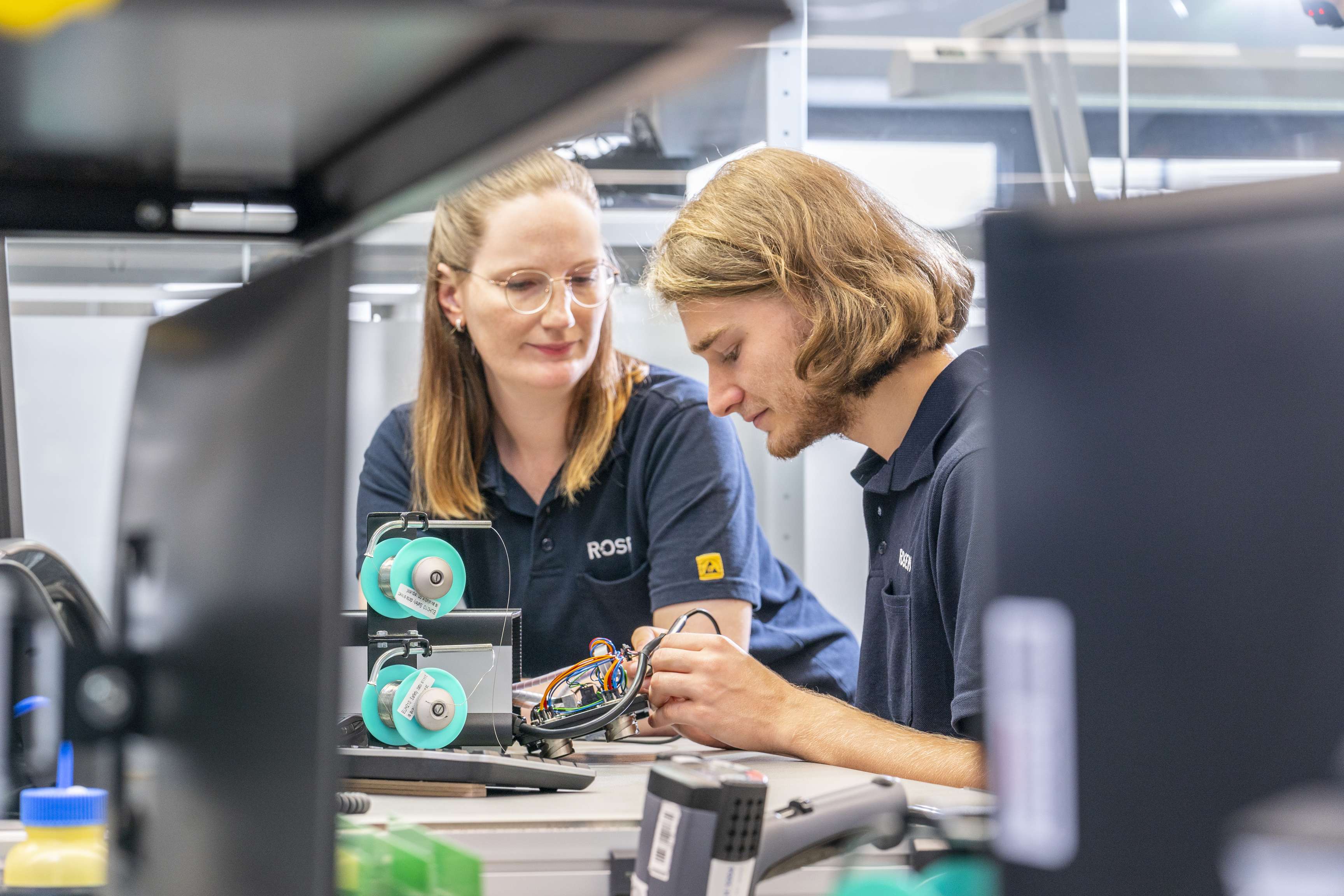 Eine Frau beaufsichtigt einen Lehrling bei seiner Arbeit im Bereich Elektronik.