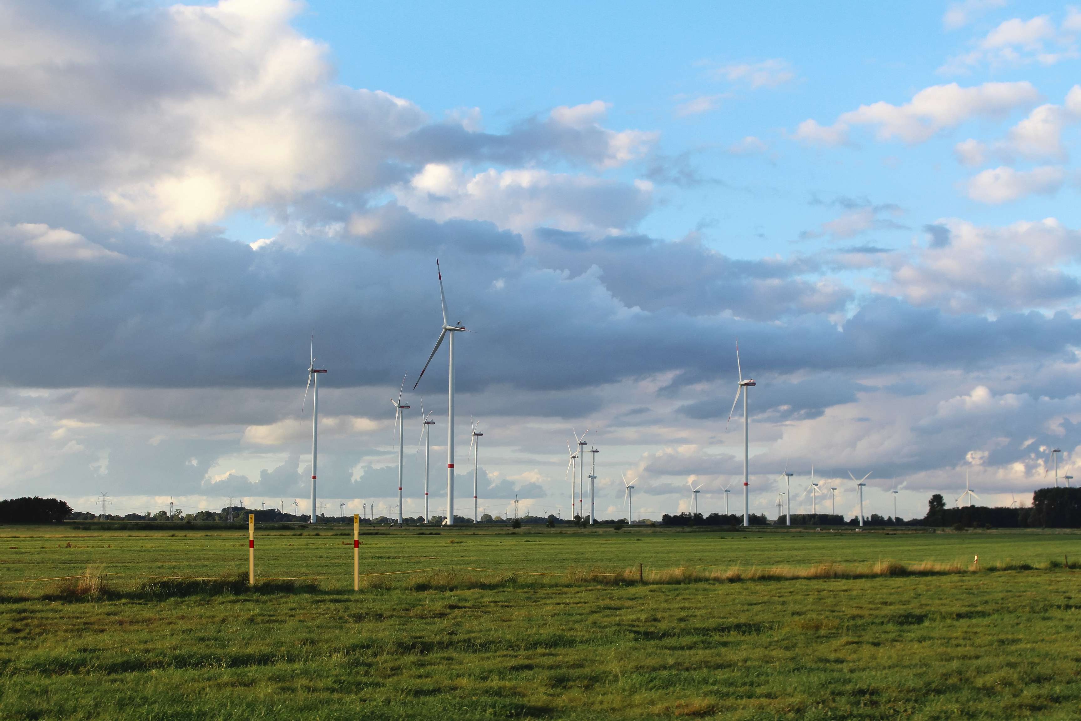 A landscape with wind turbines and pipeline markings in the foreground.