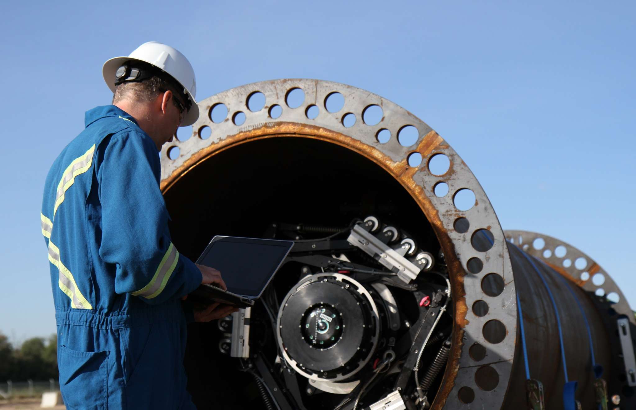 An ROSEN employee in a blue overall holding a notebook prepared a pipeline for loading.