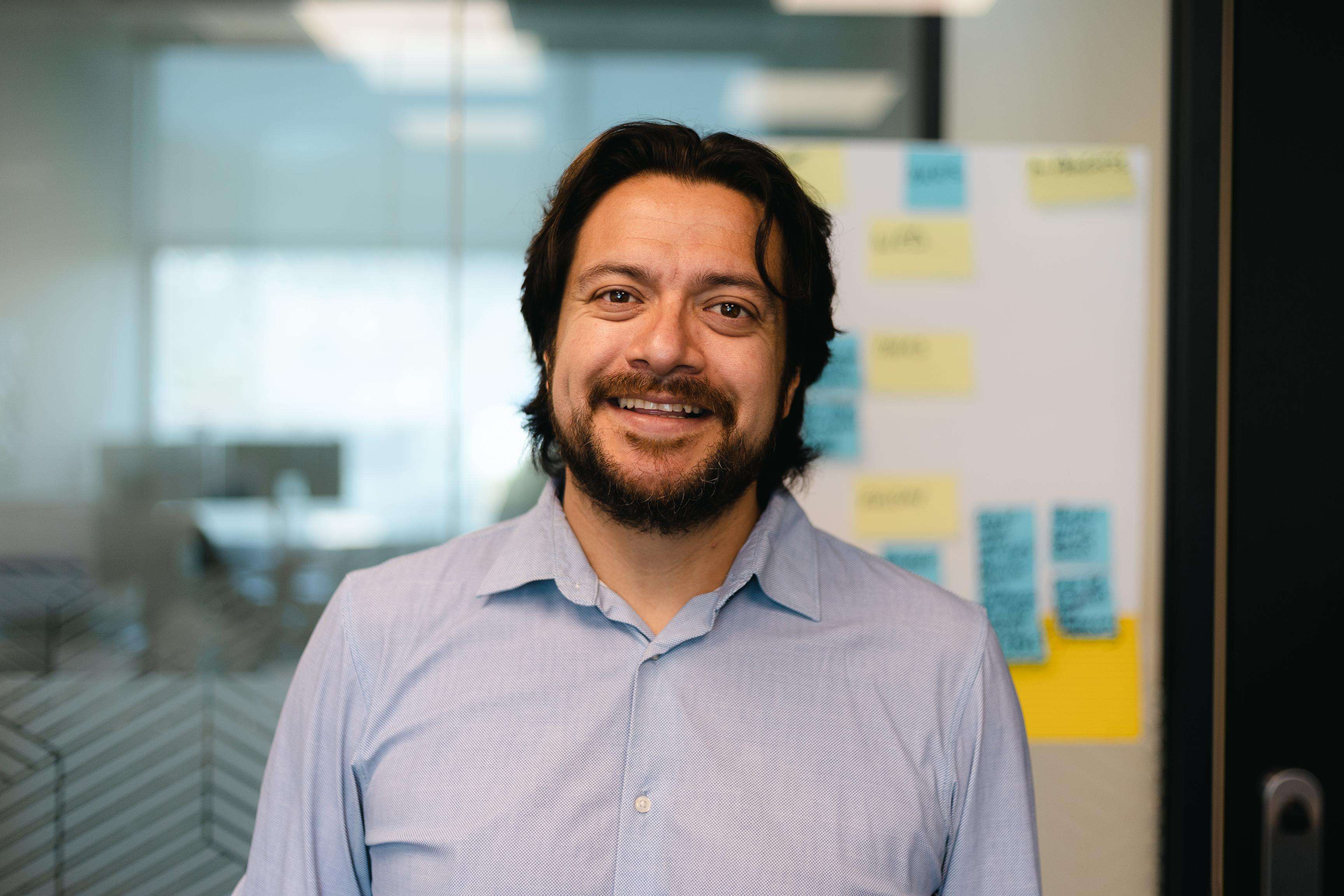 A man standing in an office space and smiling into the camera.