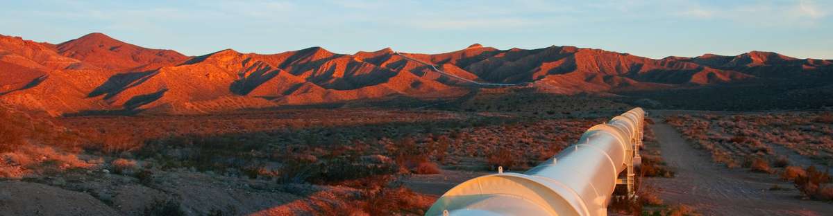 Pipeline leads through dry hilly landscape at sunset.