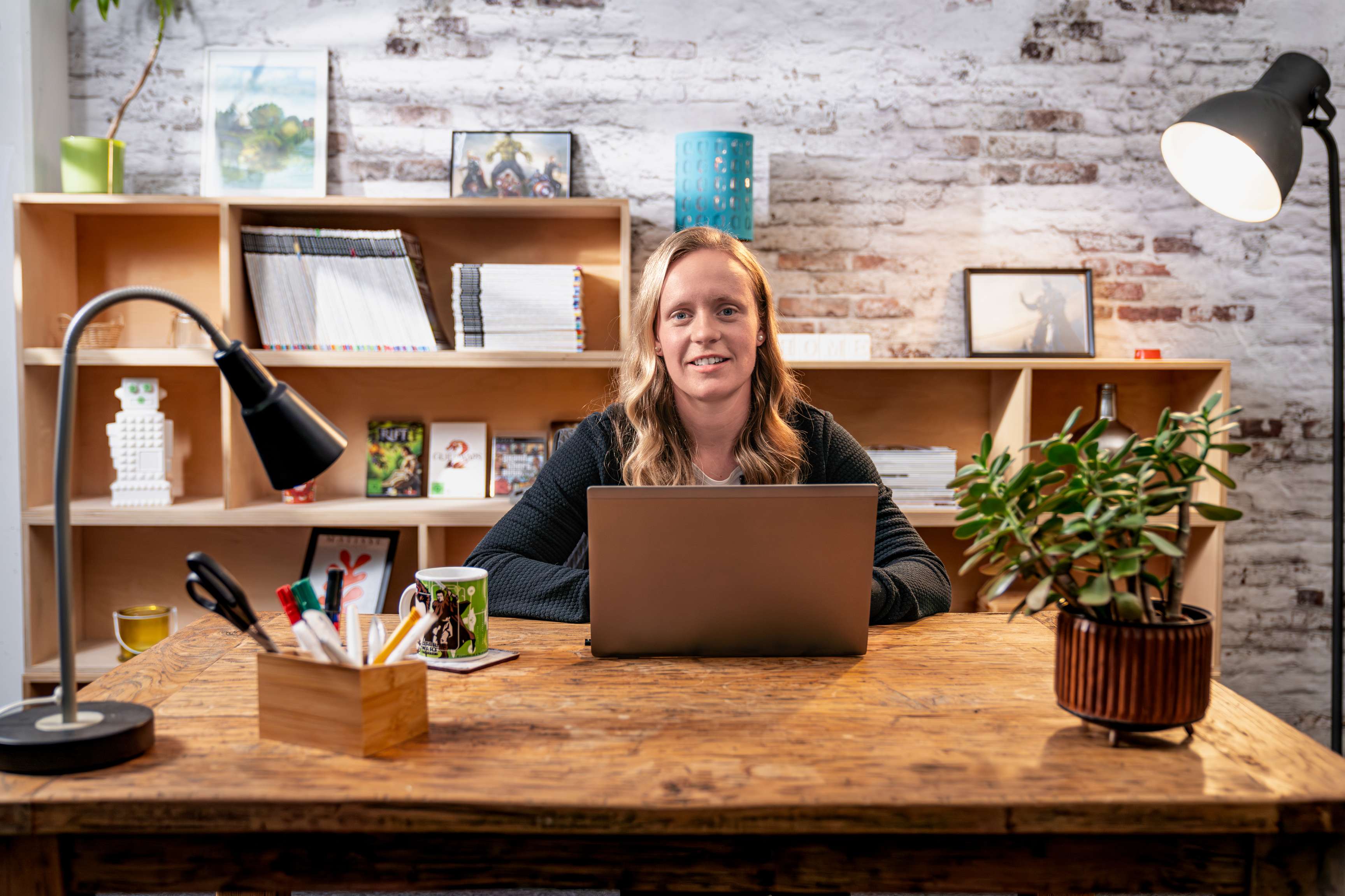 Eine Frau sitzt an einem Schreibtisch und lächelt in die Kamera.