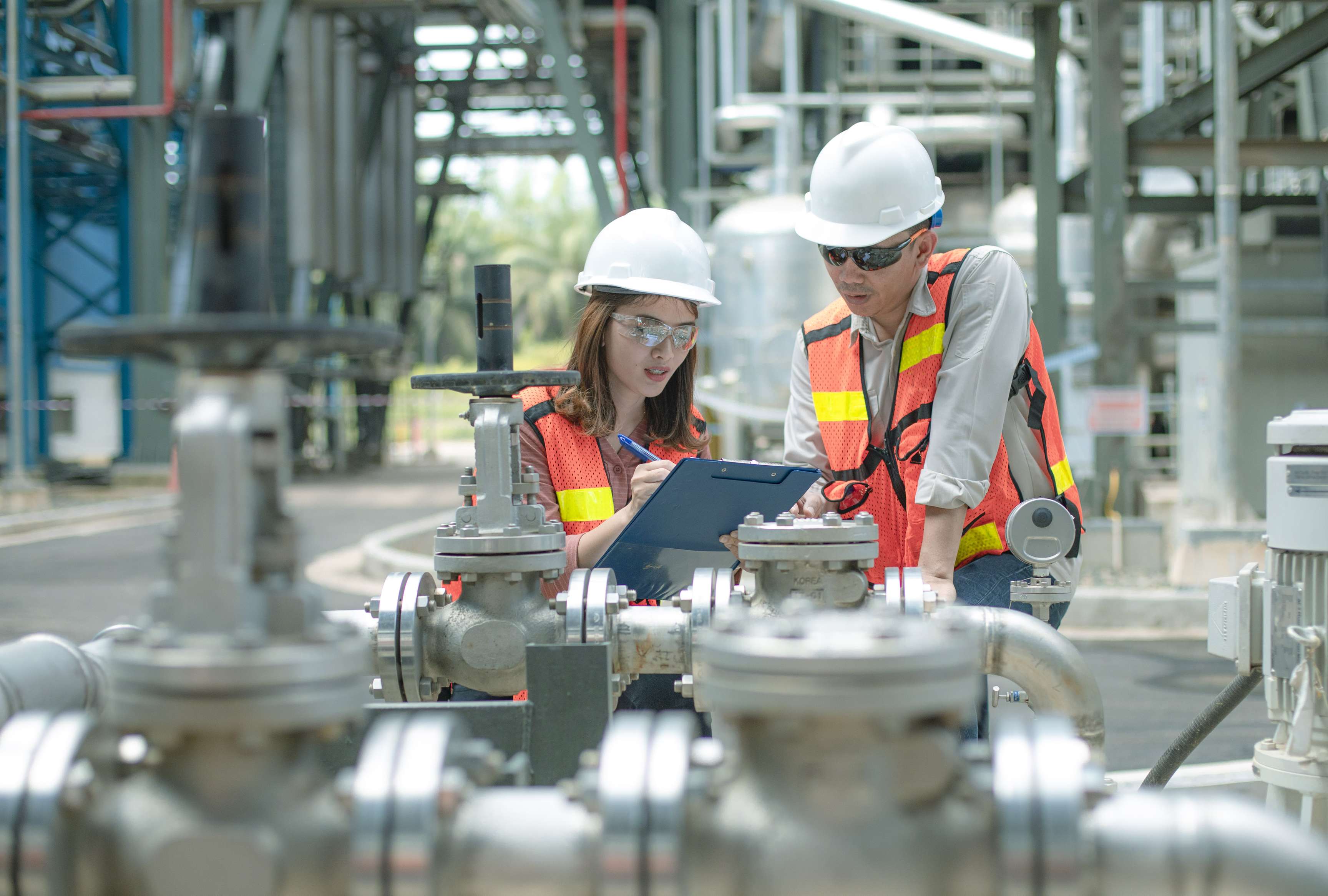 Two employees with protective equipment work together on a clipboard.