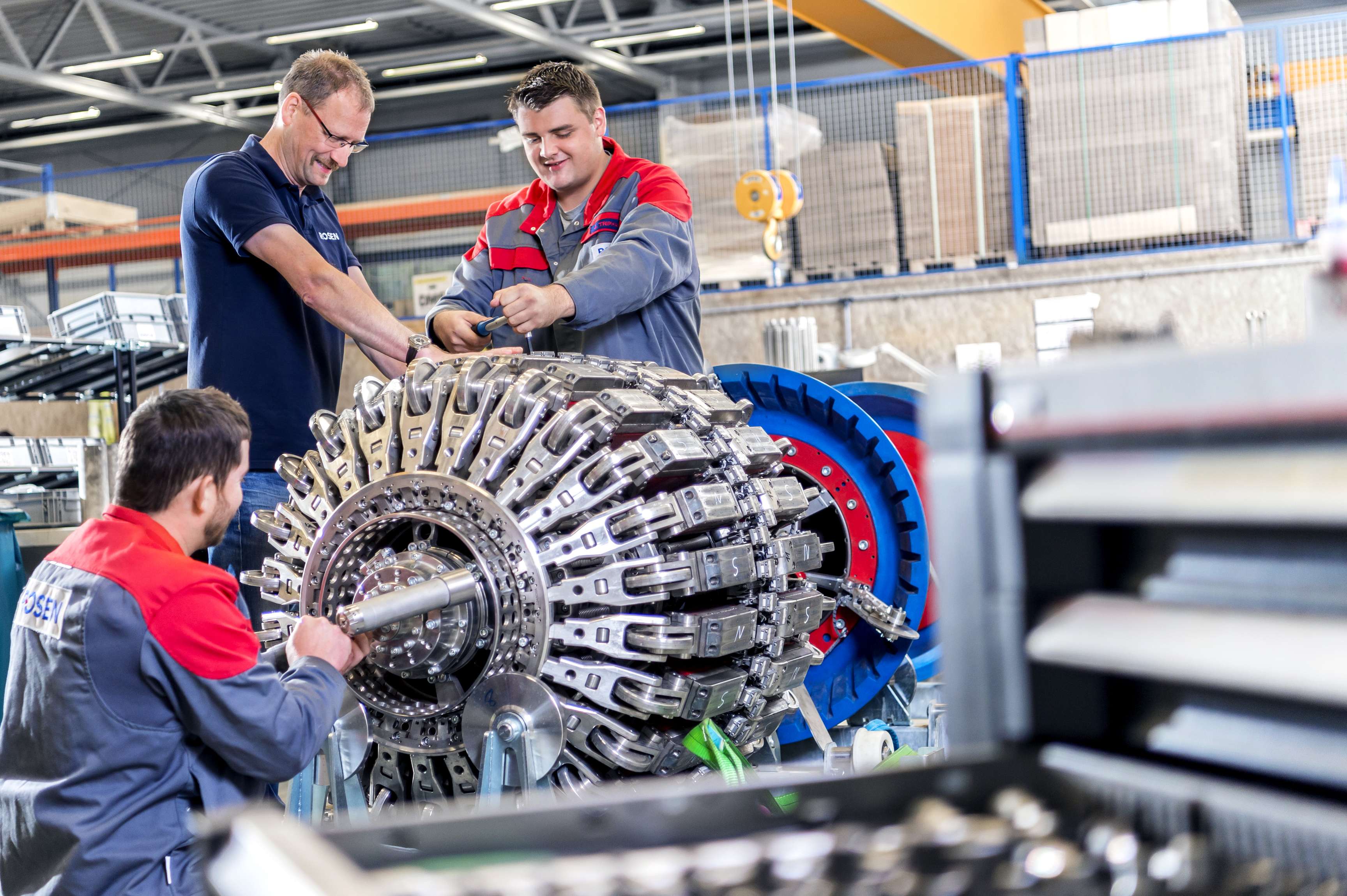 Drei Arbeiter stehen an einem Tool in der Fabrikhalle.