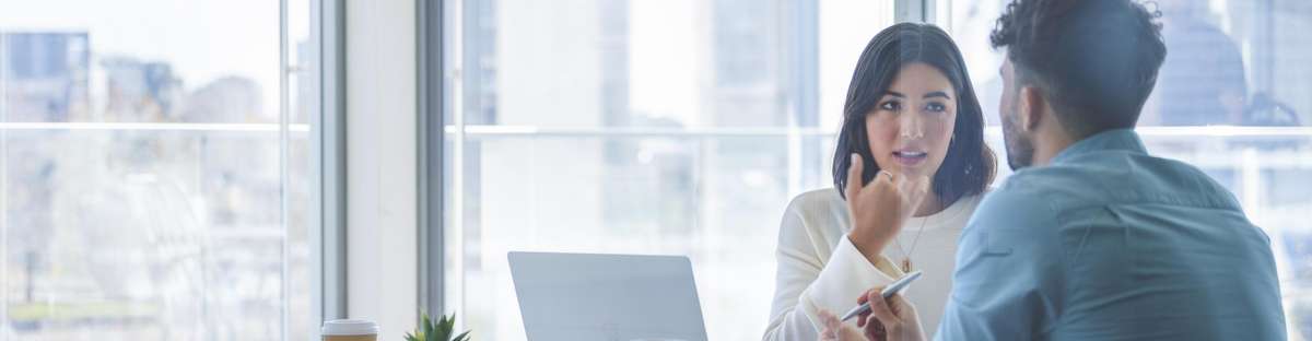 Two people sitting in a meeting room talking to each other.