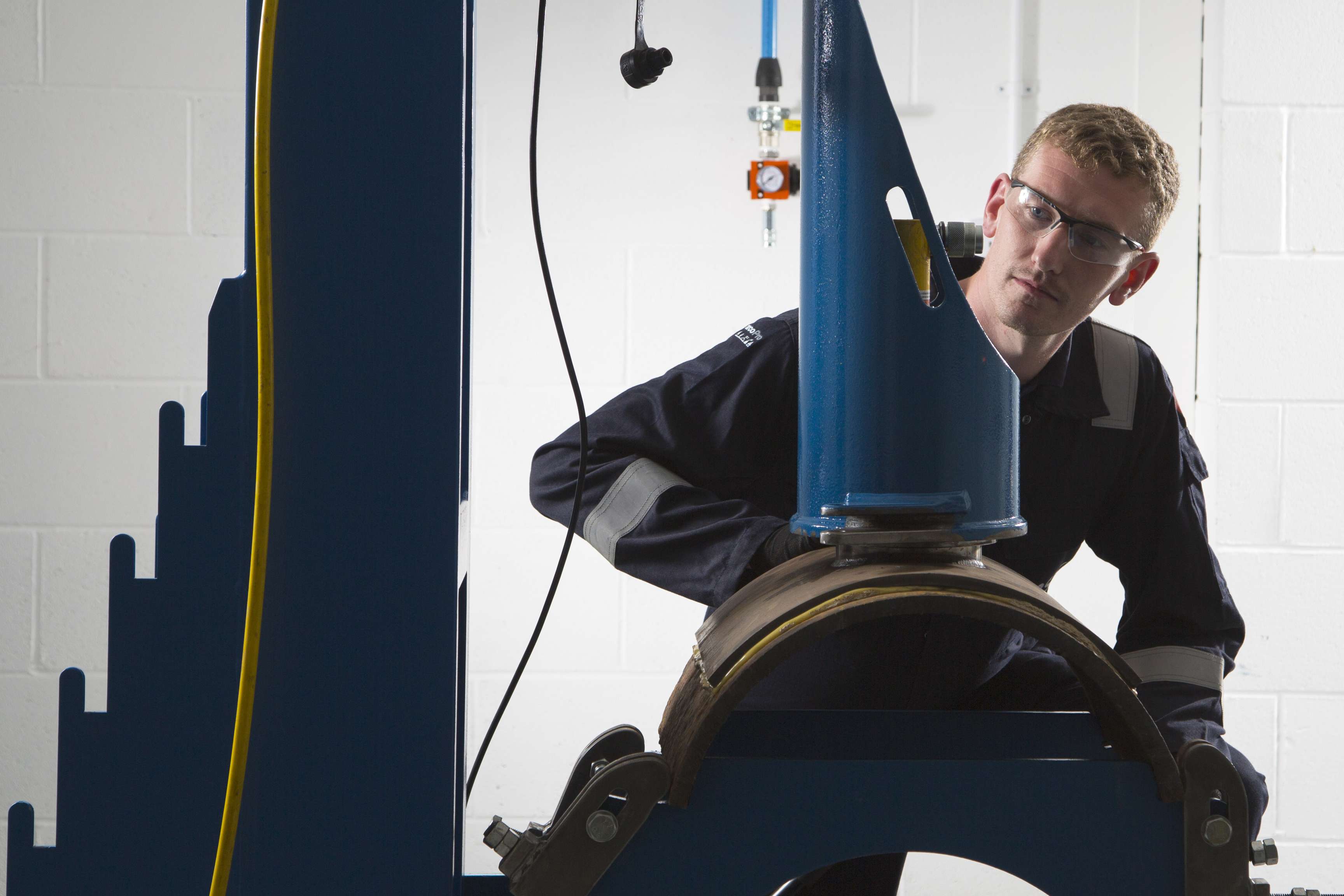 Employee sitting in front of a device which is connected to part of a pipeline.