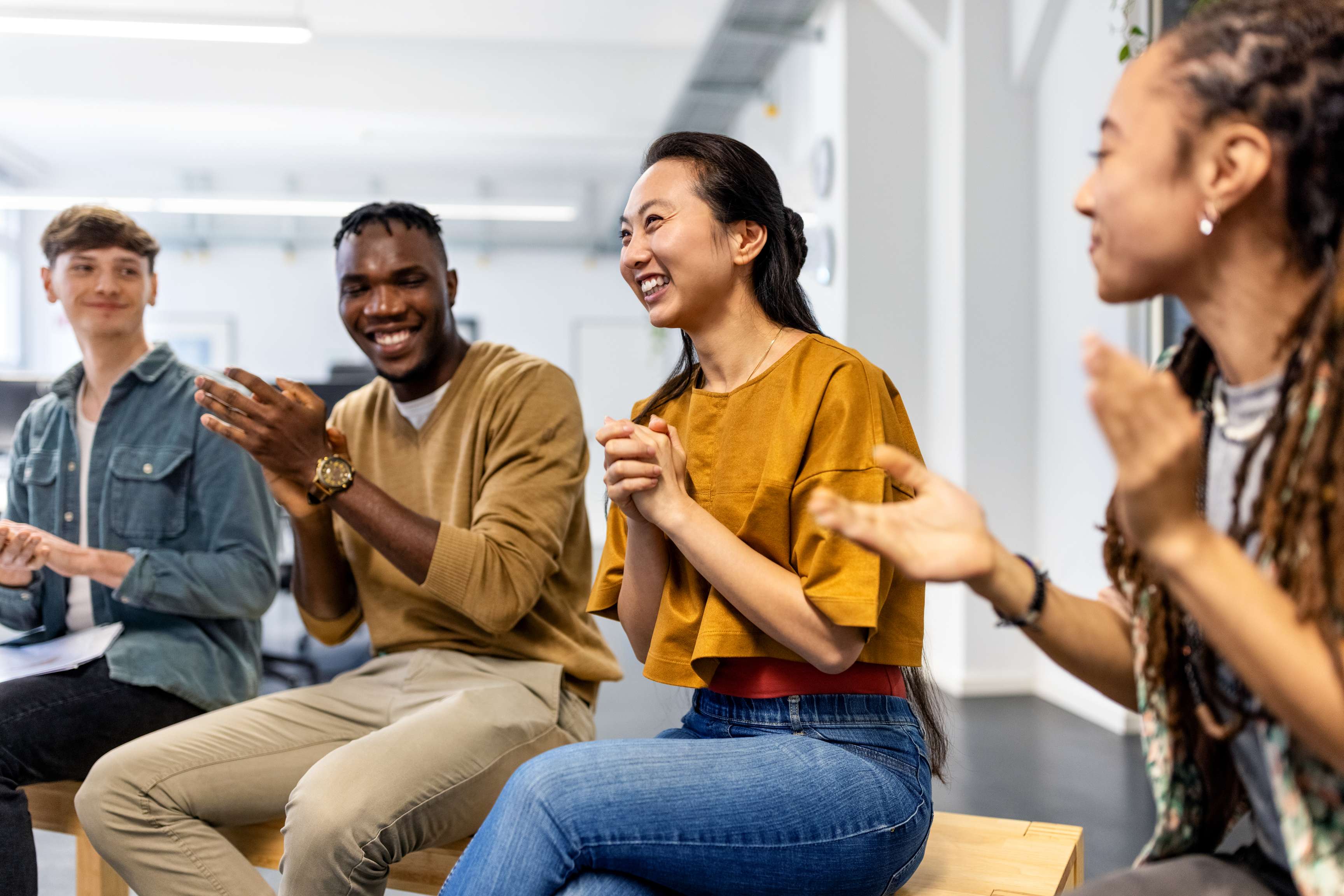 Four people sitting together in a relaxed atmosphere, looking at each other laughing and clapping their hands.