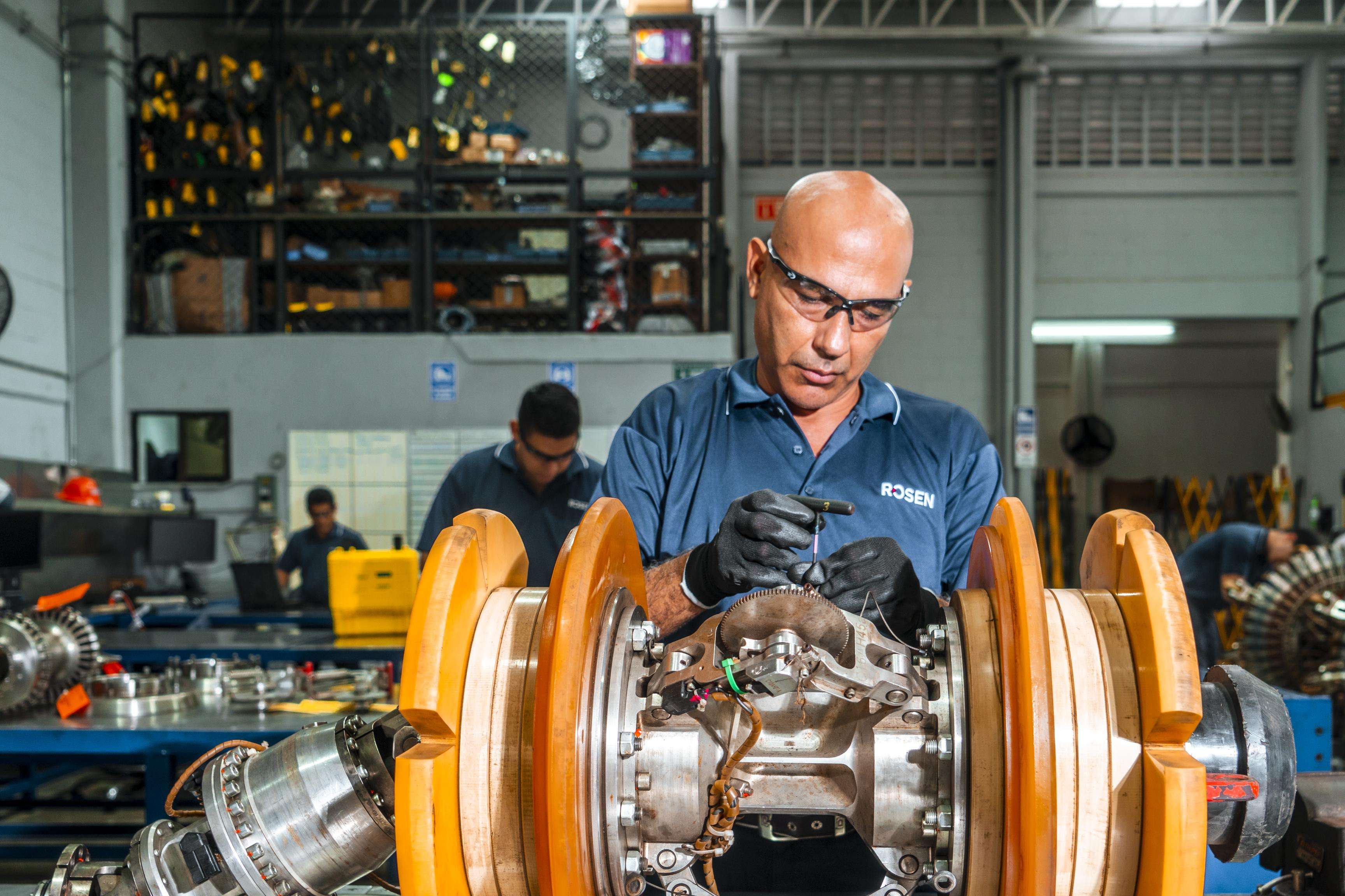 Man in a workshop setting wearing safety glasses servicing and assembling a ROSEN tool.