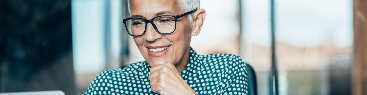 Woman wearing glasses and smiling sitting in front of laptop.