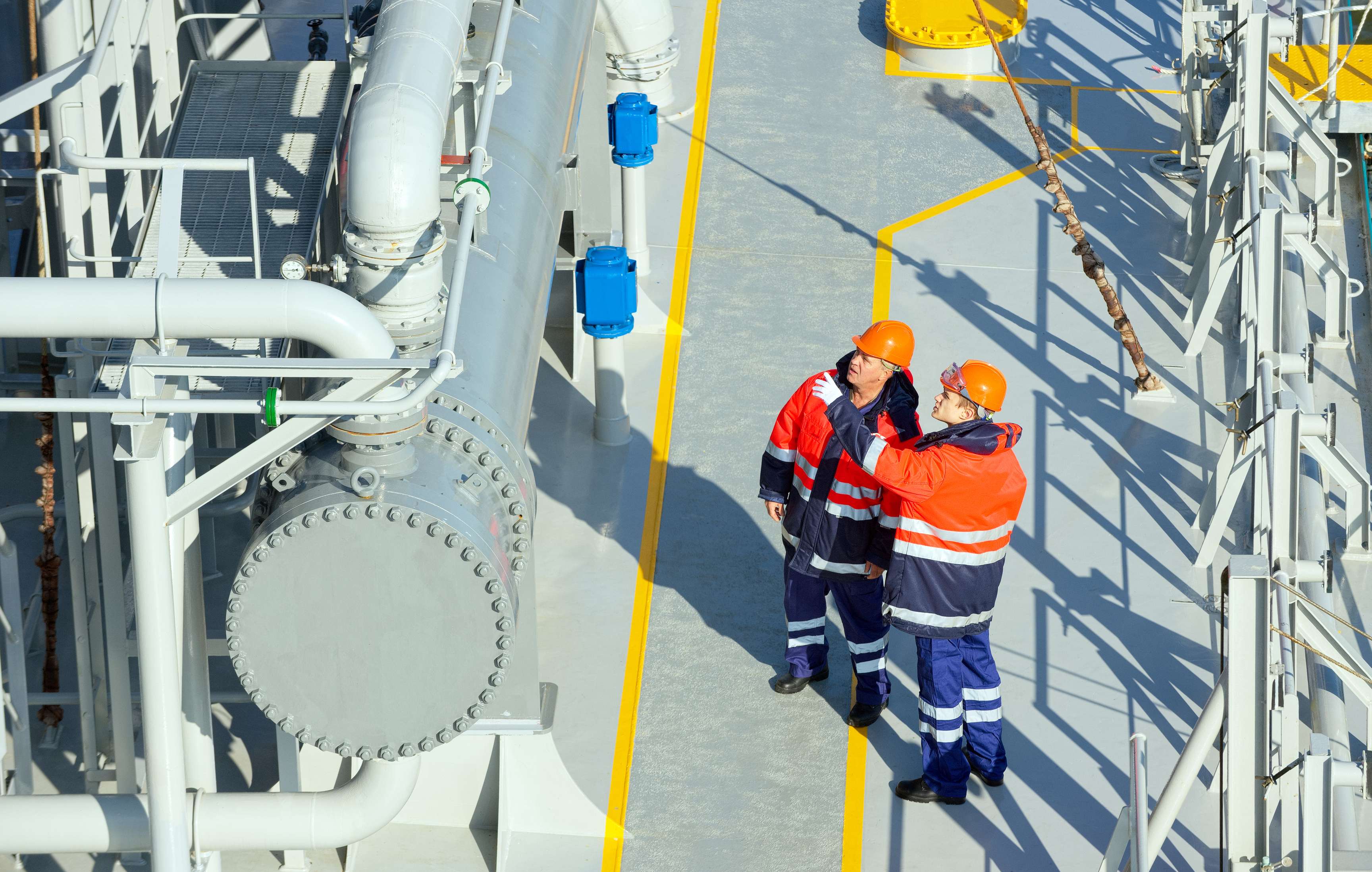 Two employees with protective equipment looking and pointing at a pipeline.