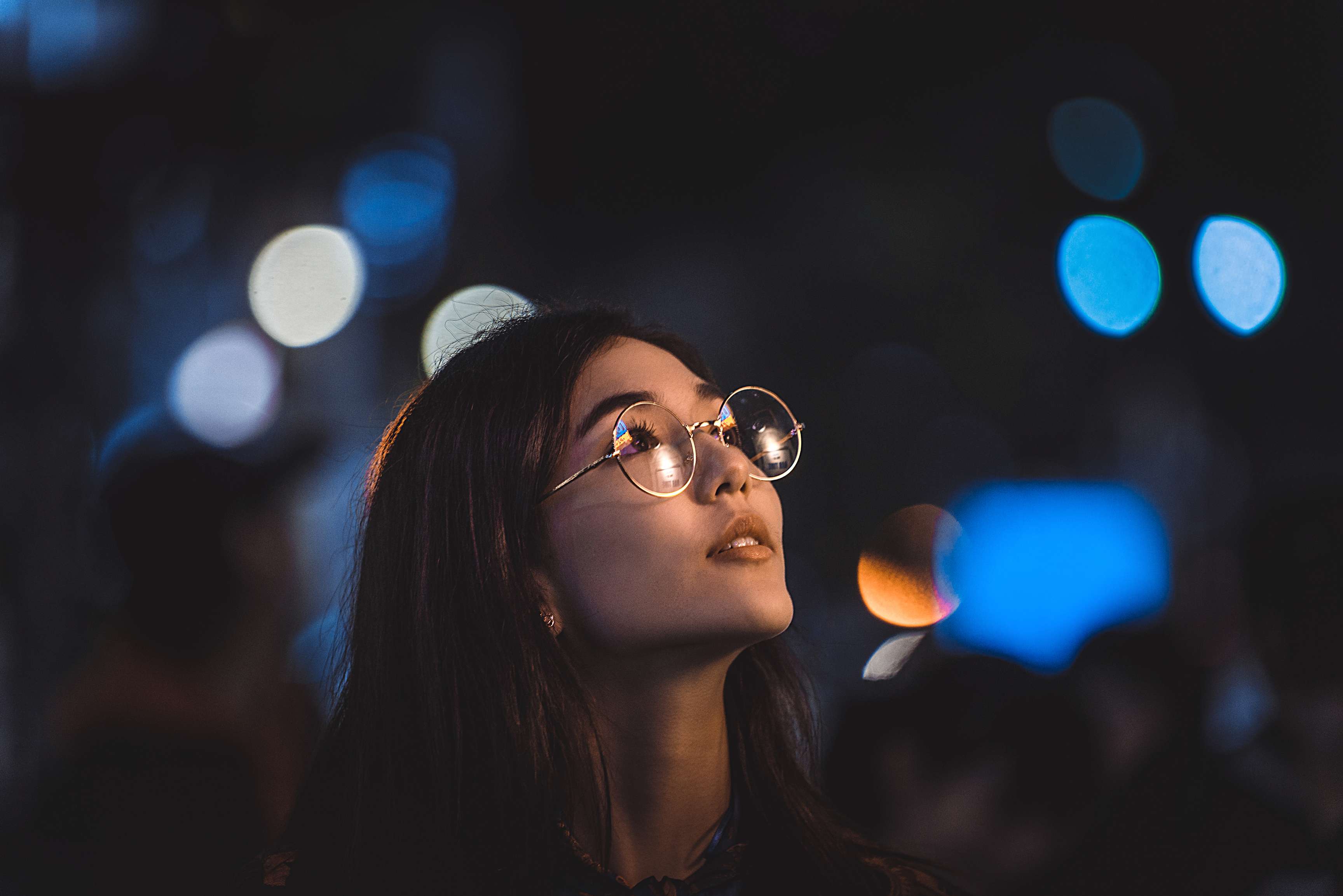 Woman wearing glasses looking to the right with a dark background.