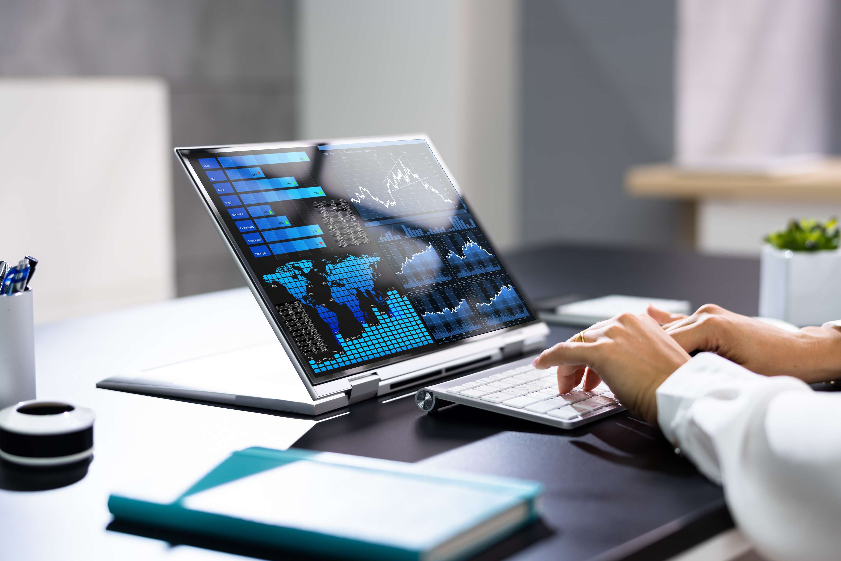 A person sits at a laptop at a desk on which various charts are displayed.