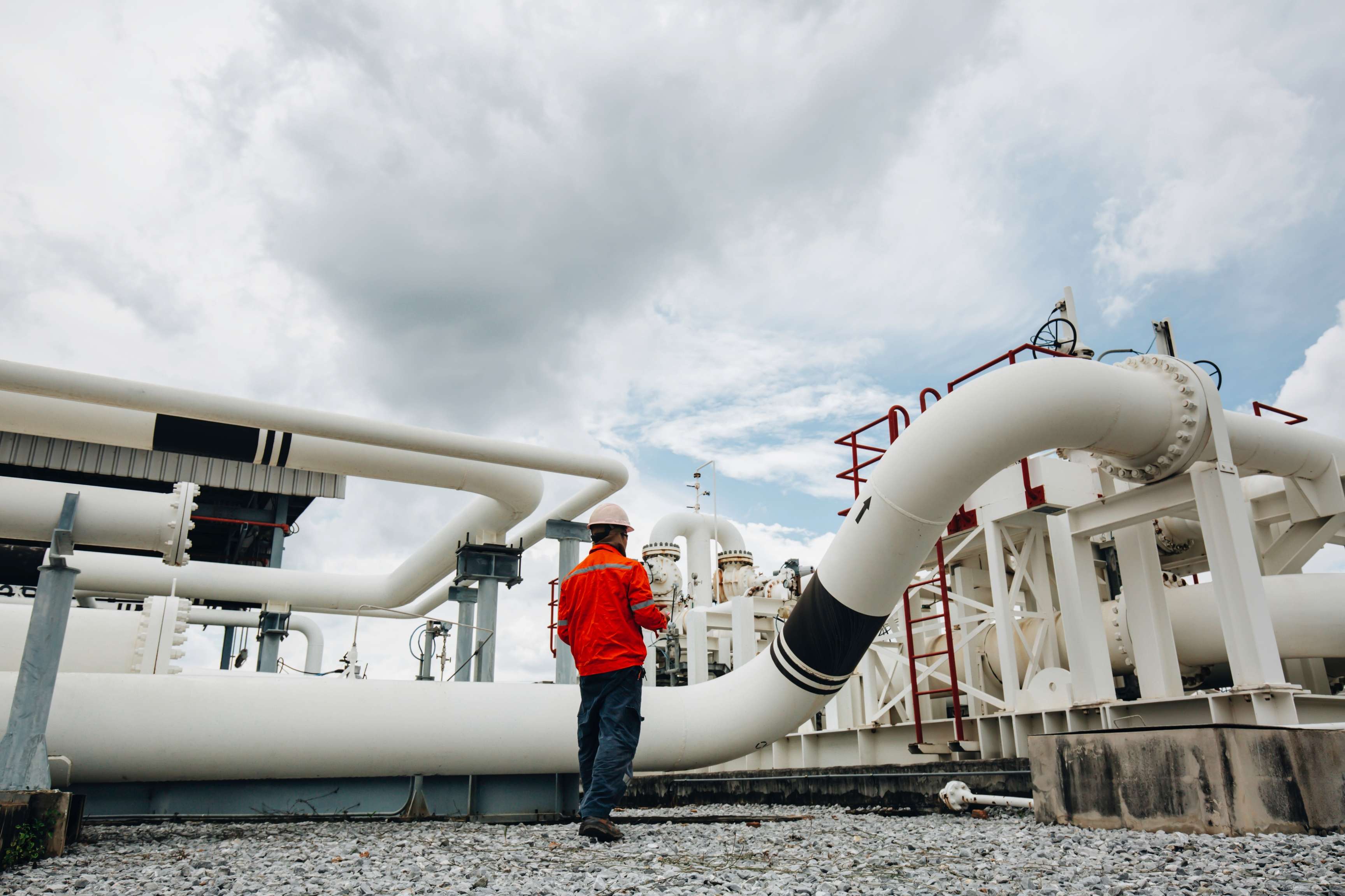 Man with safety helmet and safety clothing in front of a piping system.