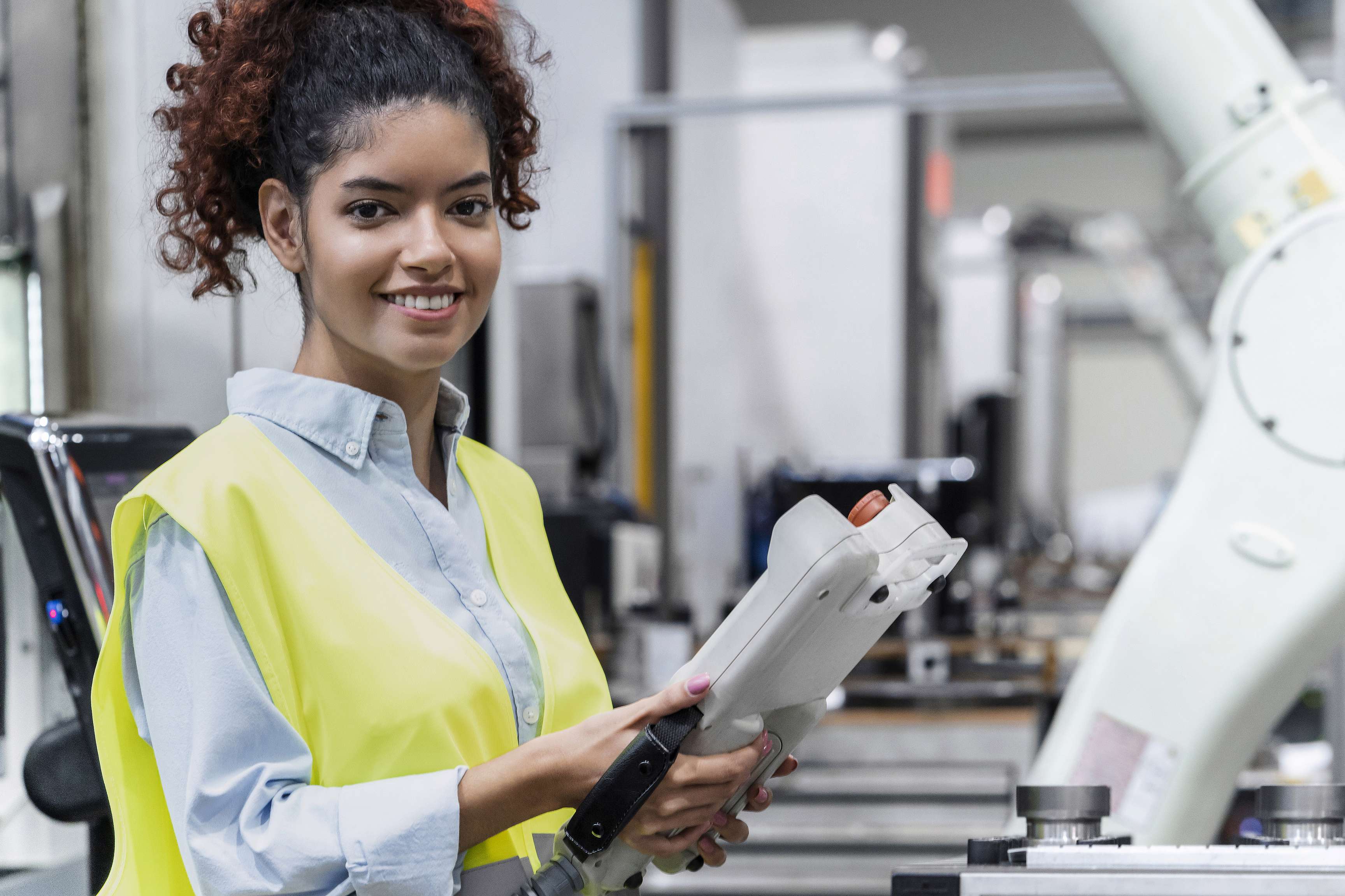 Employee smiles at camera and holds a device for a machine in her hands.