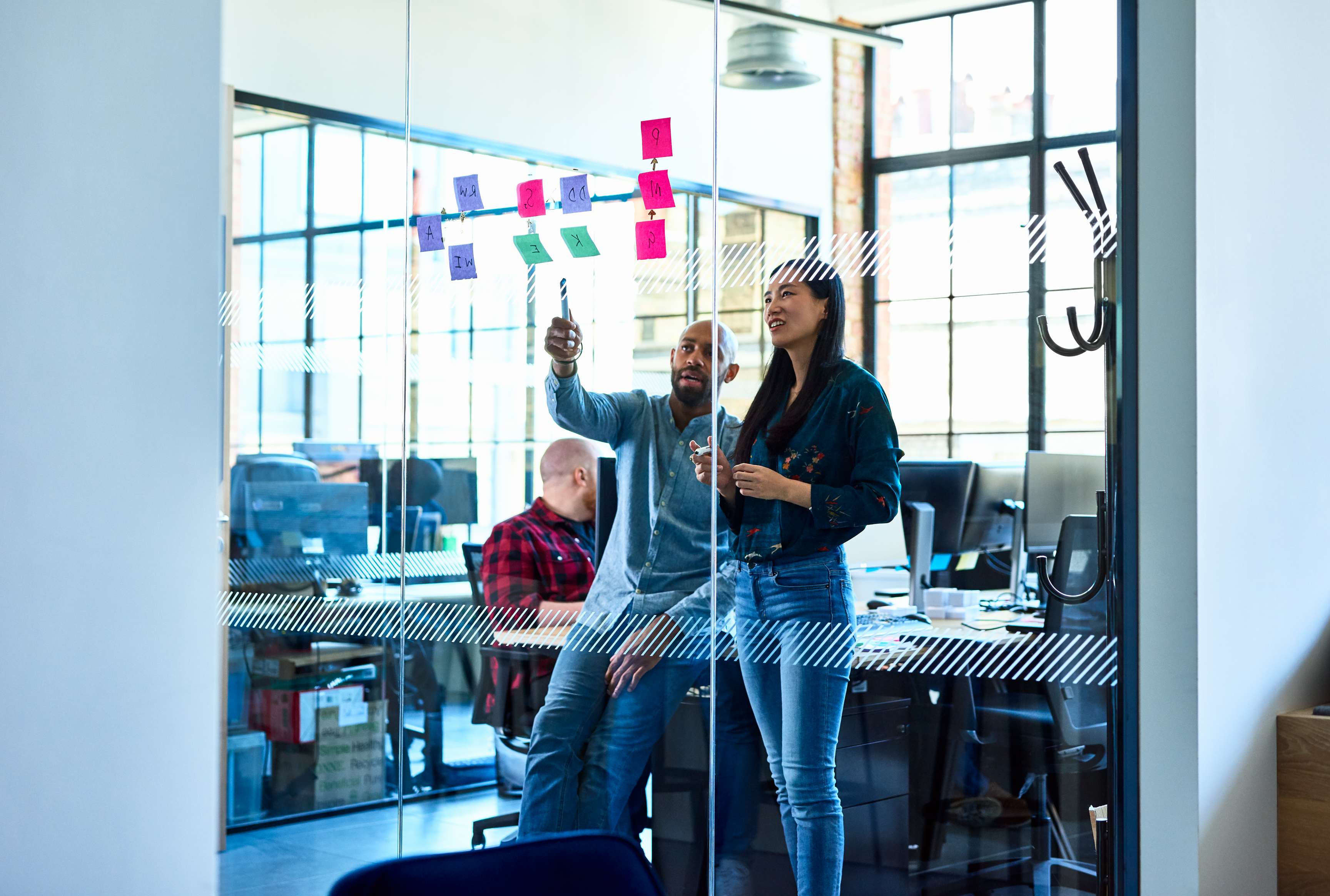 Chinese woman and male colleague in office with adhesive notes. Businessman mentoring female colleague, discussing business strategy, using sticky notes to plan and solve problems.